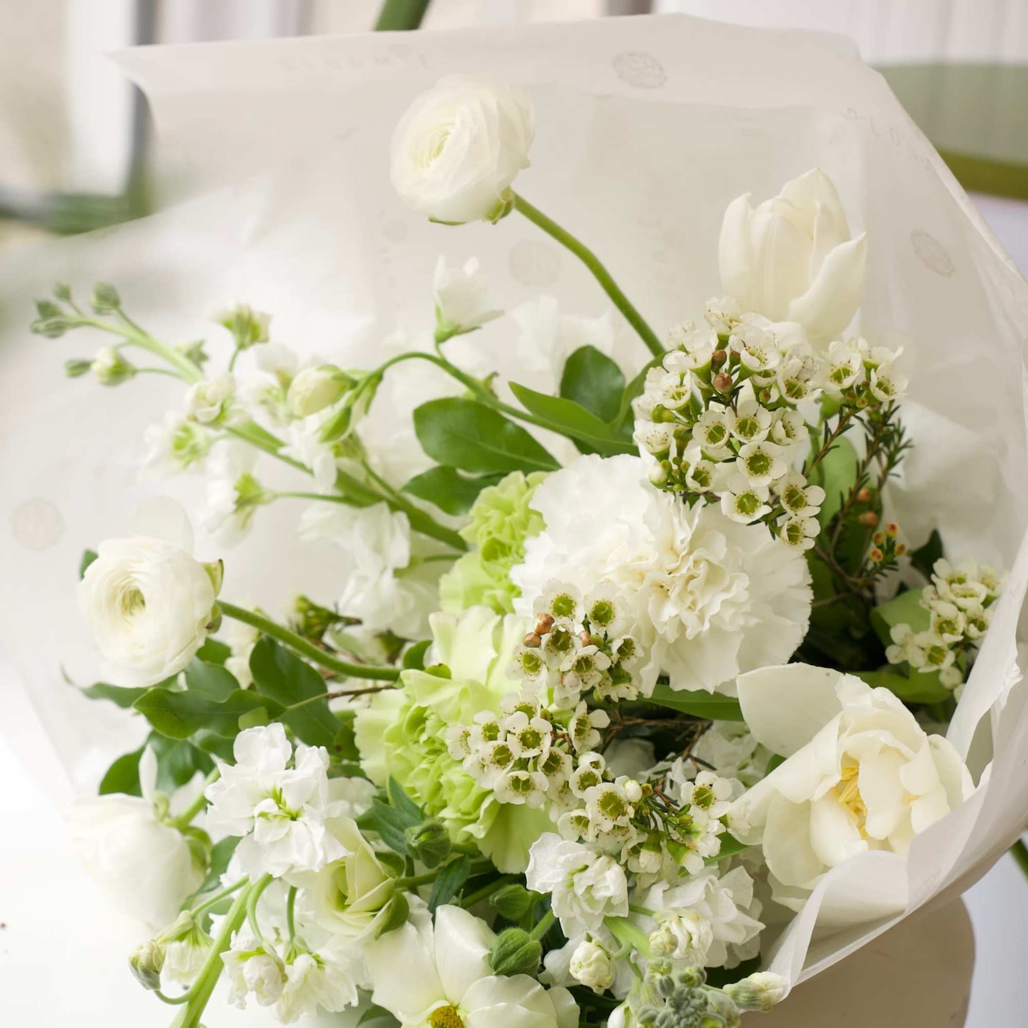 White bouquet with ranunculus, tulips, and small blossoms wrapped in paper
