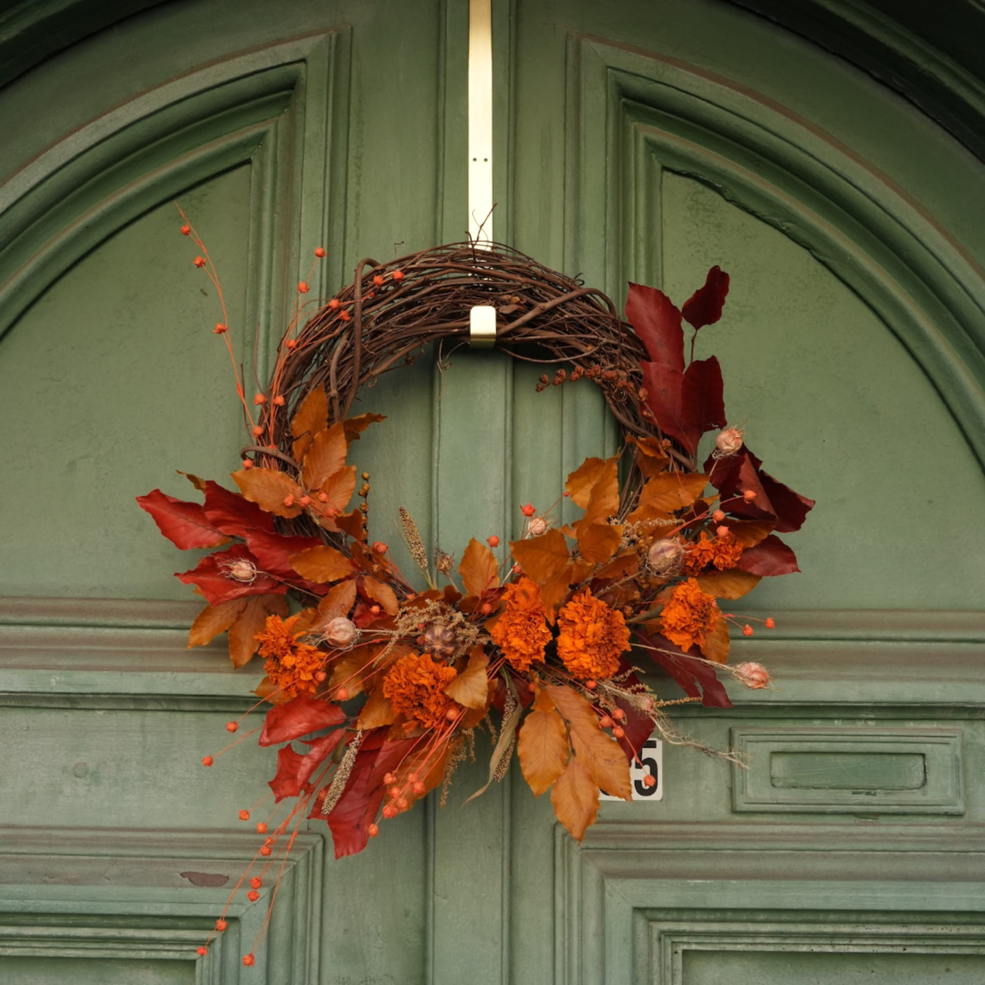 Autumn wreath with orange and red foliage on a green door