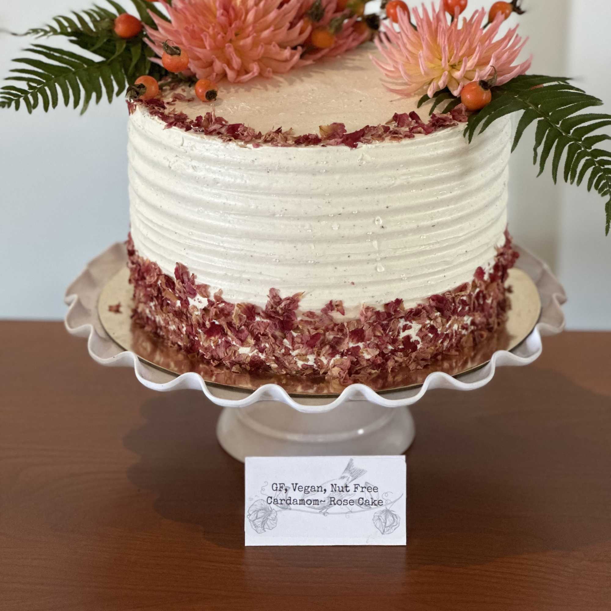 White frosted cake topped with pink flowers and fern fronds