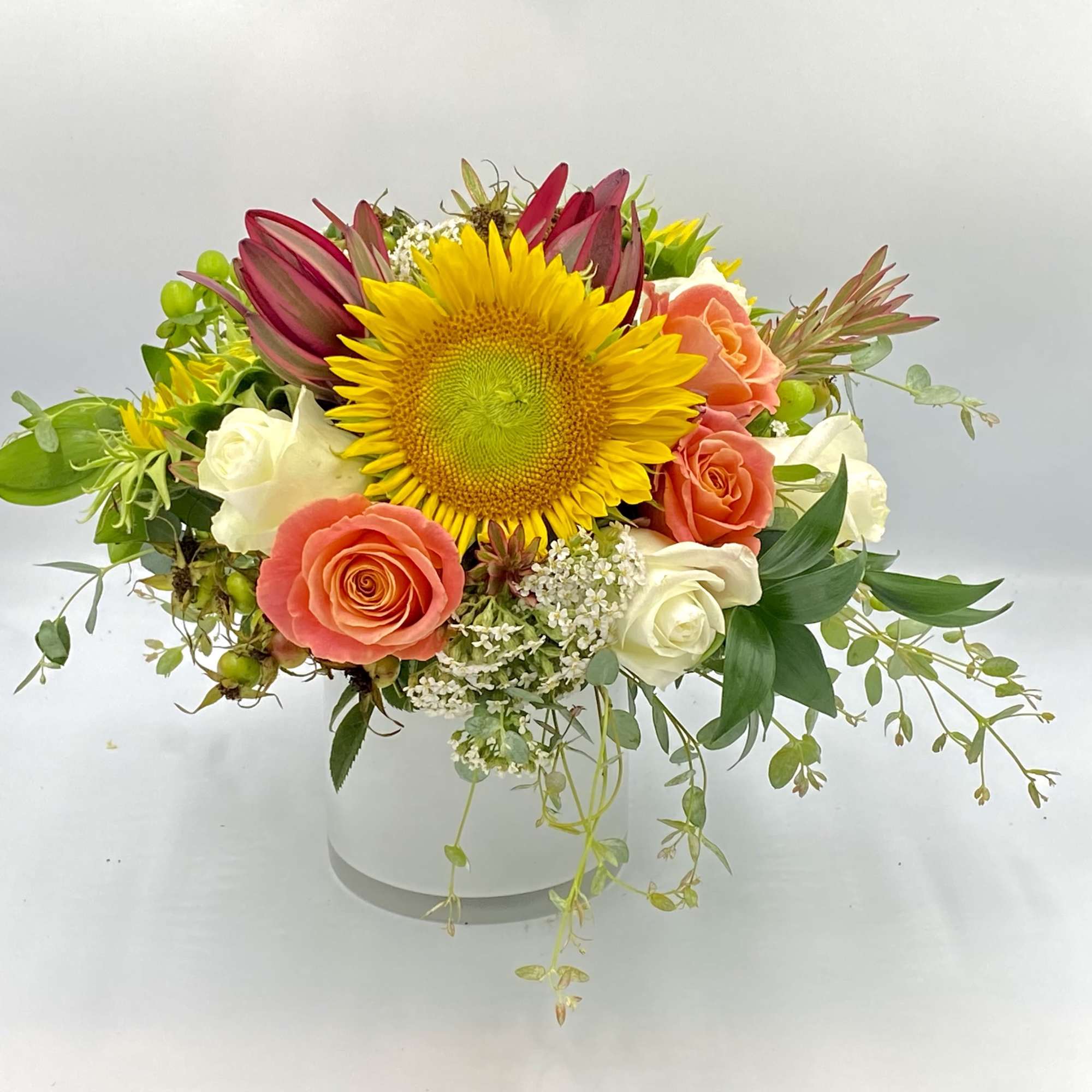 Mixed bouquet with a sunflower, roses, and white blooms in a white vase