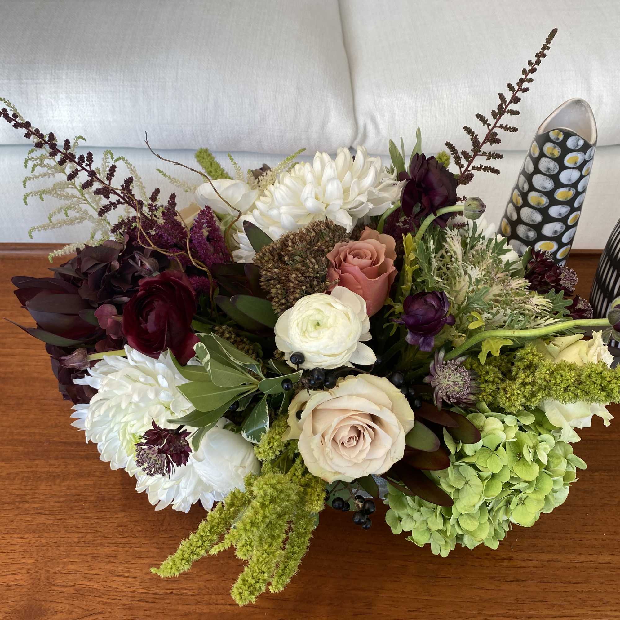 Low floral arrangement with white, blush, burgundy, and green blooms in decorative vases