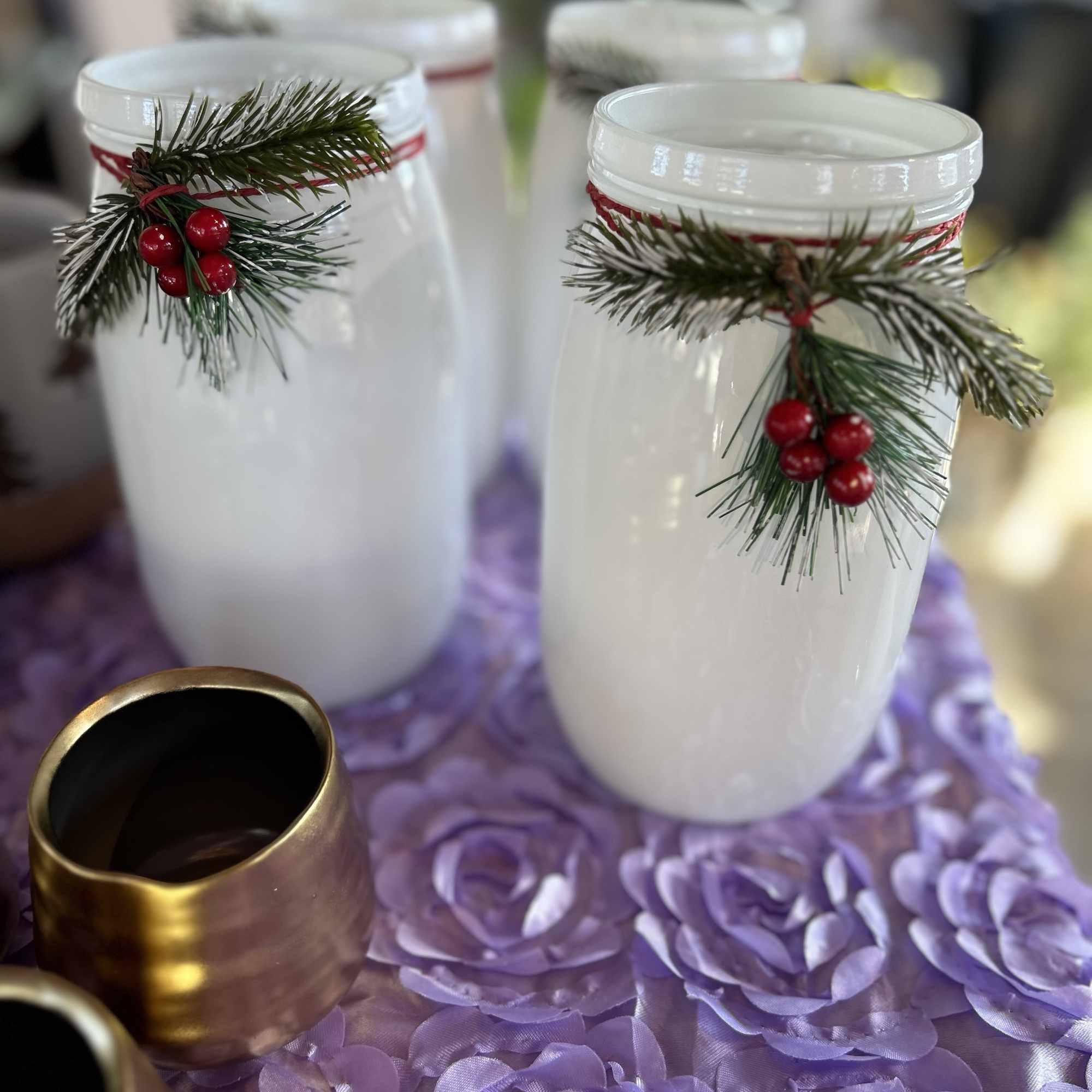 White jars decorated with pine sprigs and red berries on a purple table runner