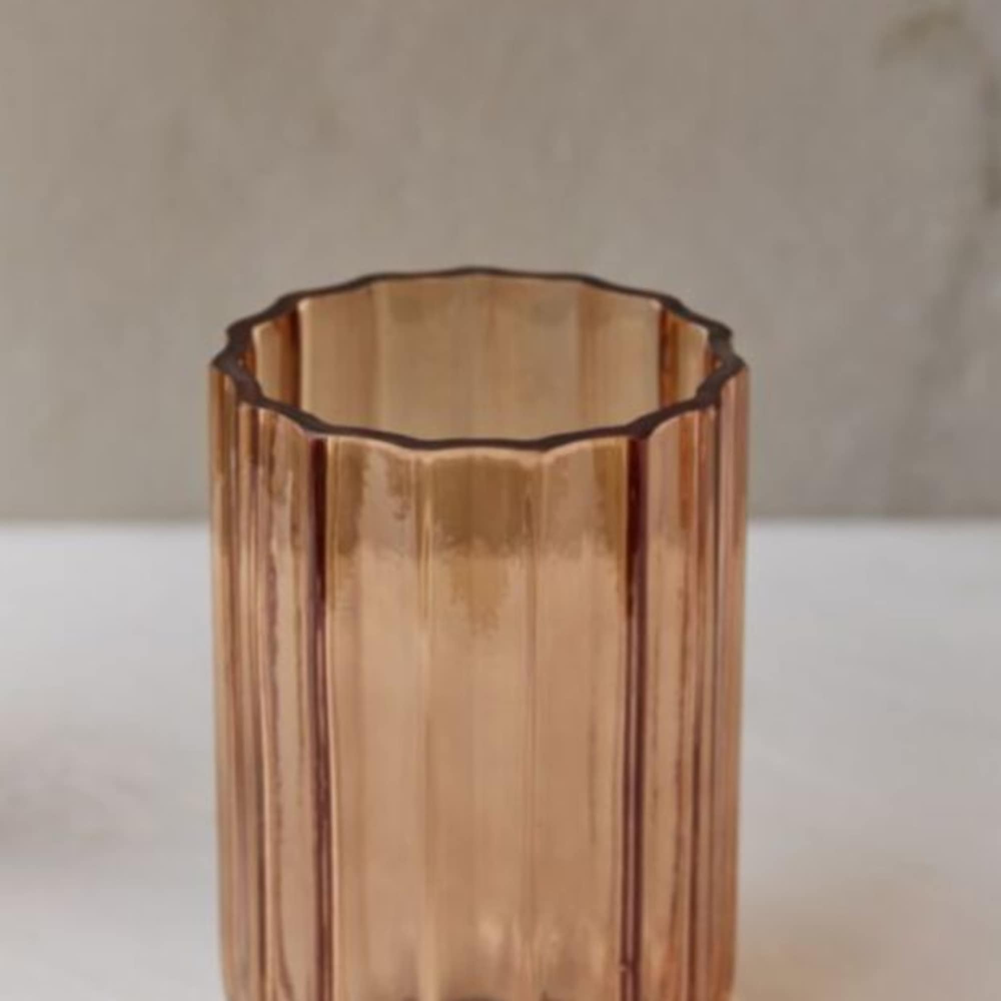 Amber ribbed glass vase on a white surface with a branch above