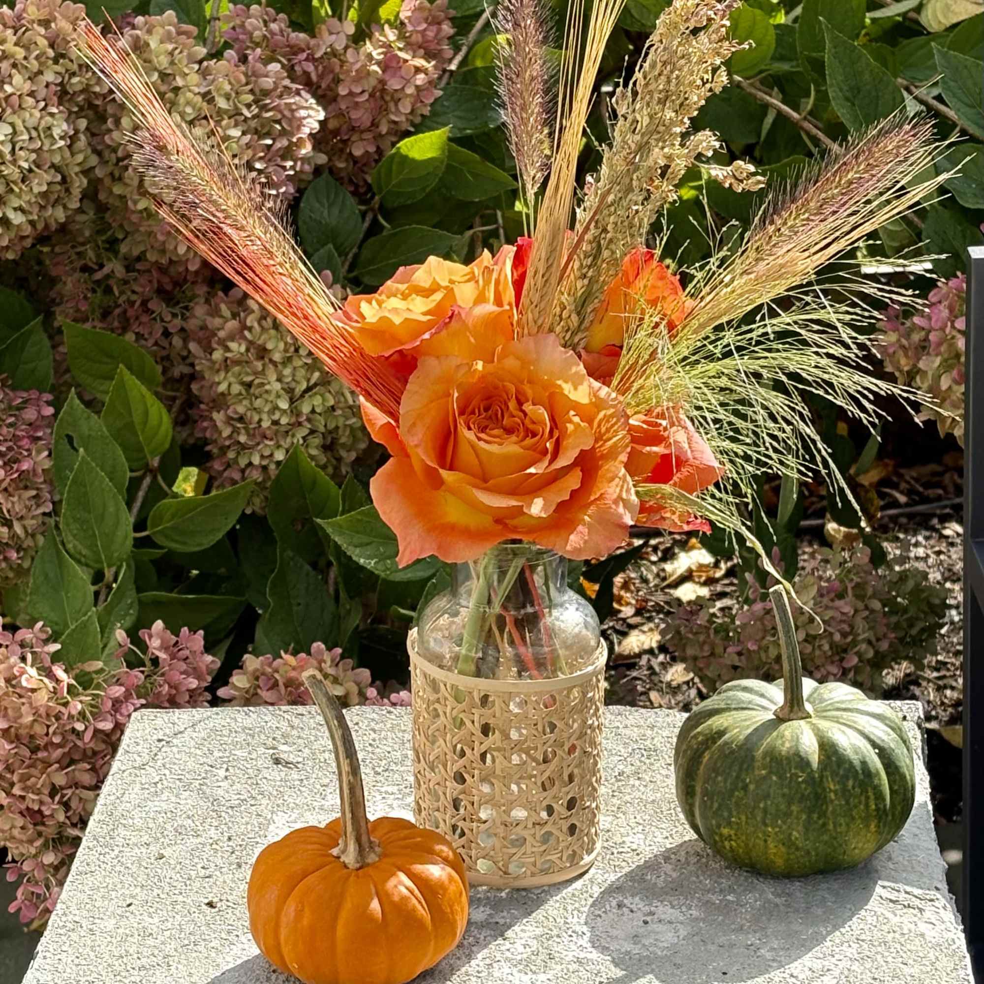 Orange rose arrangement in a glass bottle with pumpkins on a stone ledge
