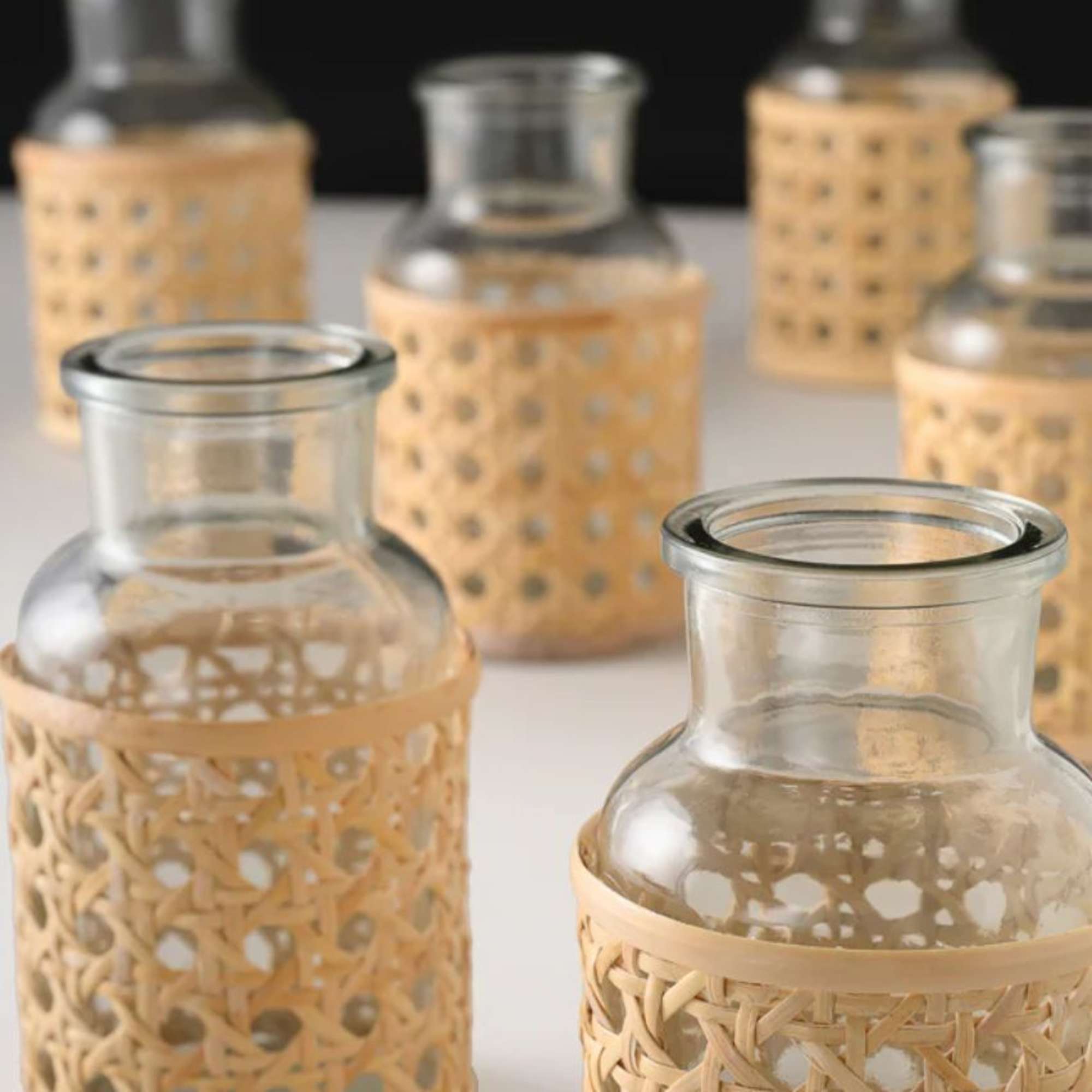 Five small glass vases with woven bamboo sleeves on a white surface