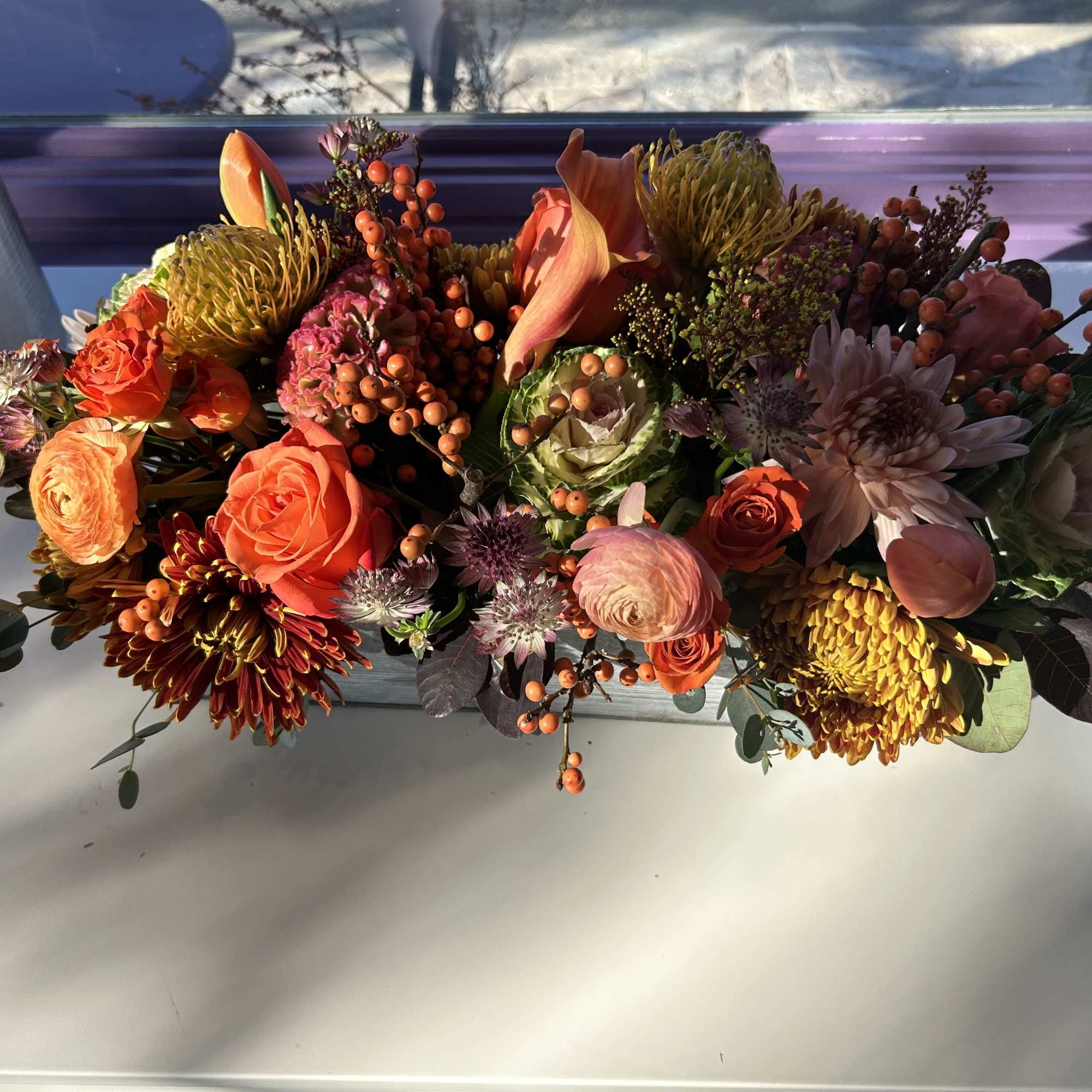 Low floral arrangement with orange and pink blooms in a rectangular container