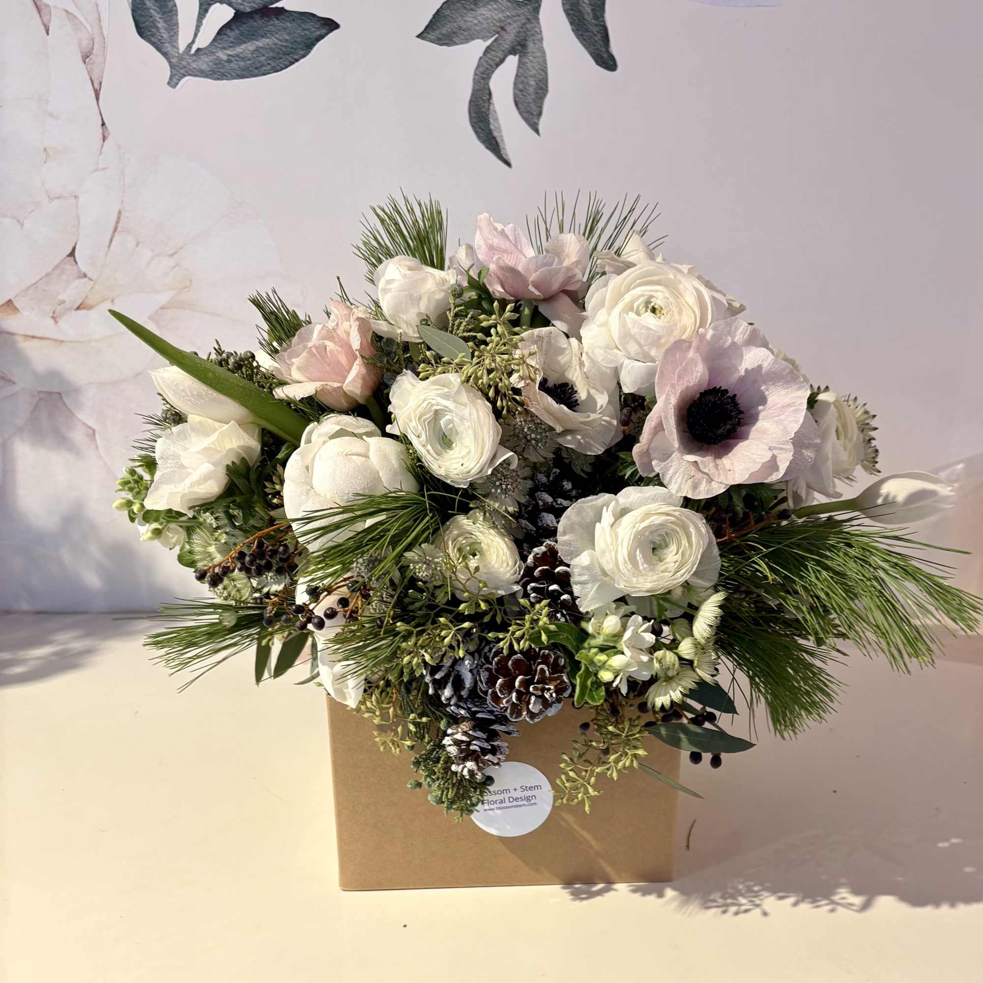 White and blush floral arrangement in a brown box with pinecones