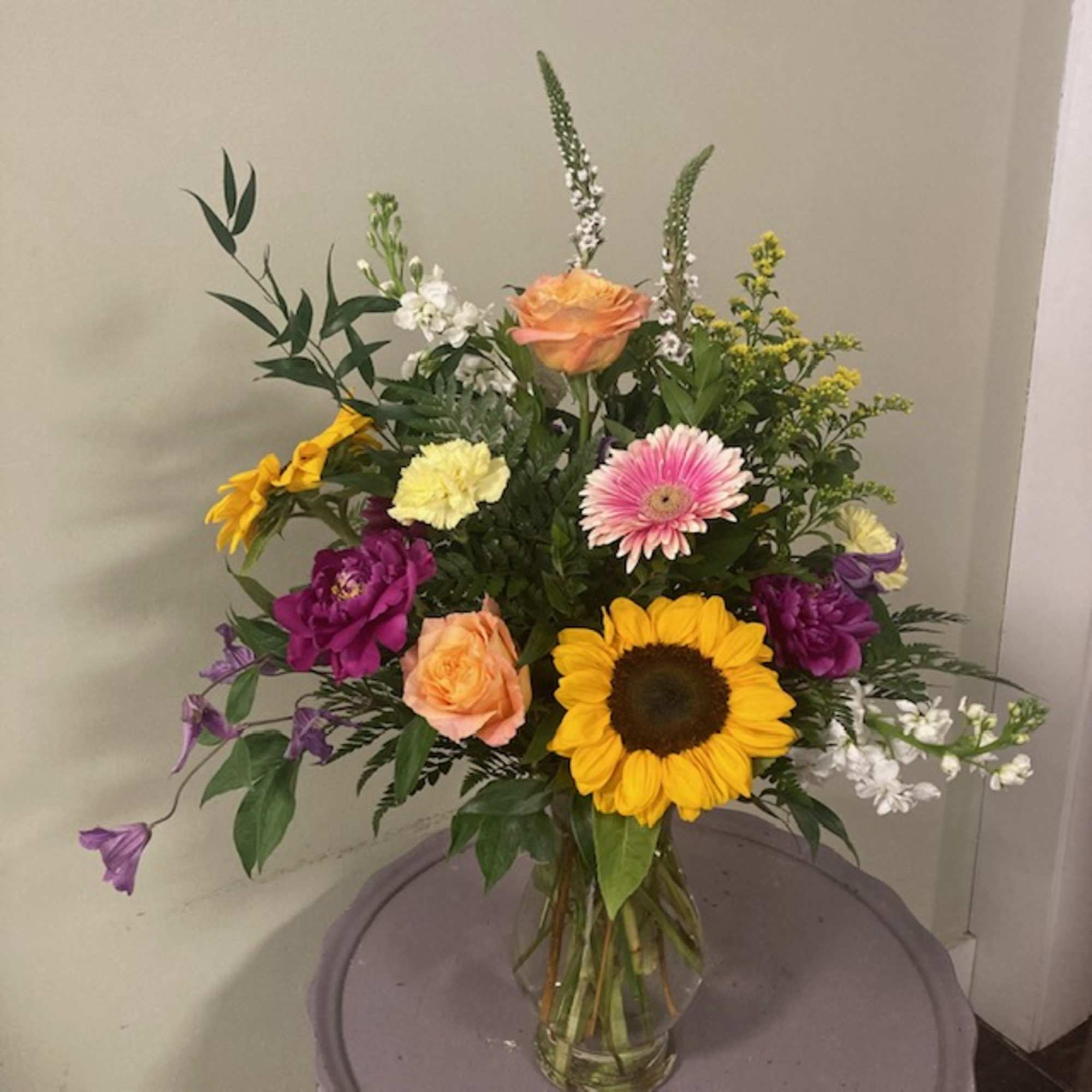 Mixed bouquet with sunflowers, roses, and gerbera daisies in a glass vase