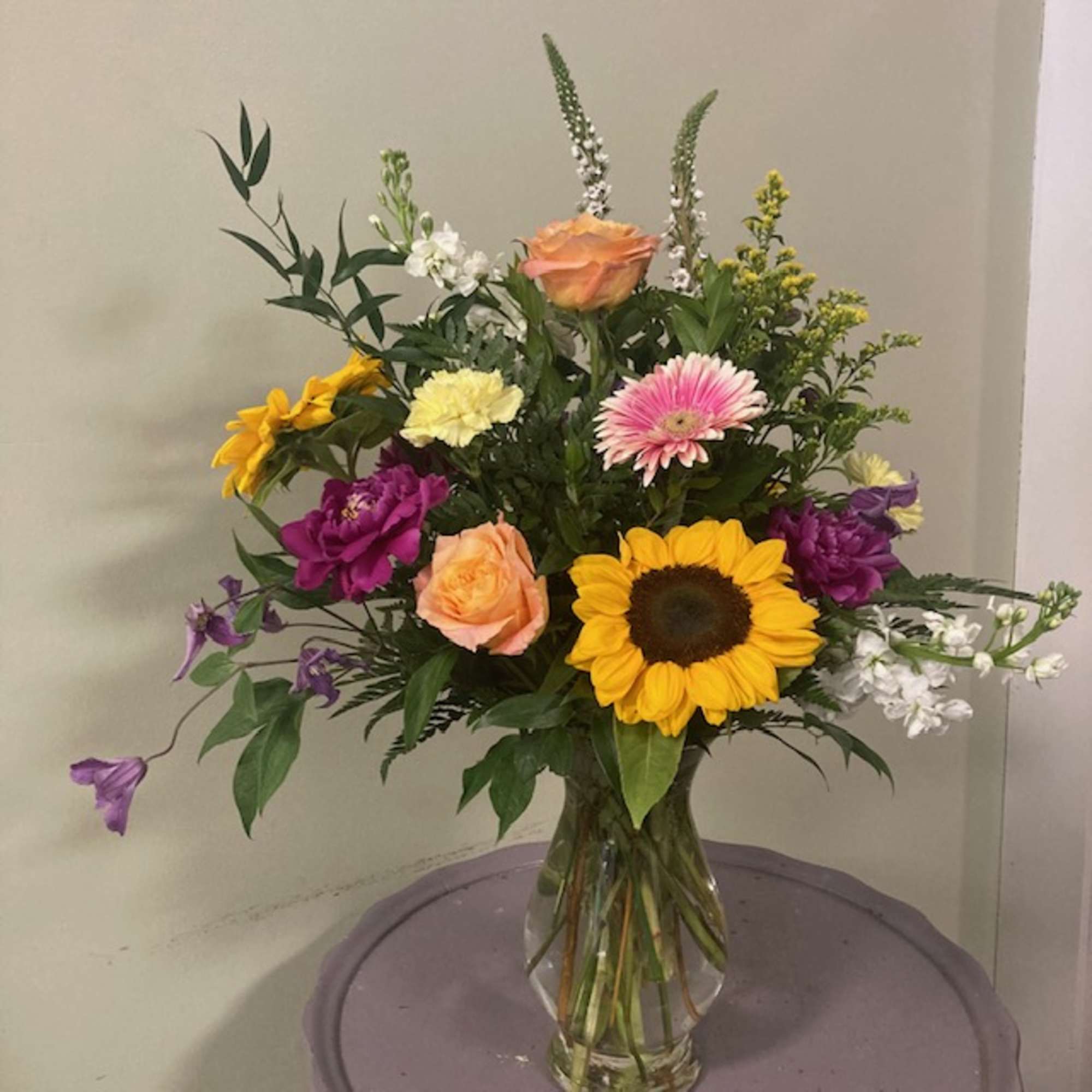 Mixed bouquet with sunflower, roses, gerbera daisy, and carnations in a glass vase