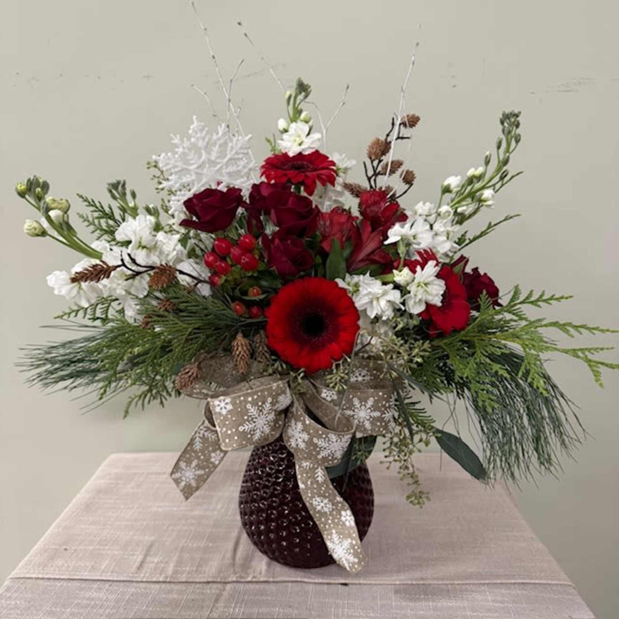 Red and white floral arrangement in a dark vase with a snowflake ribbon