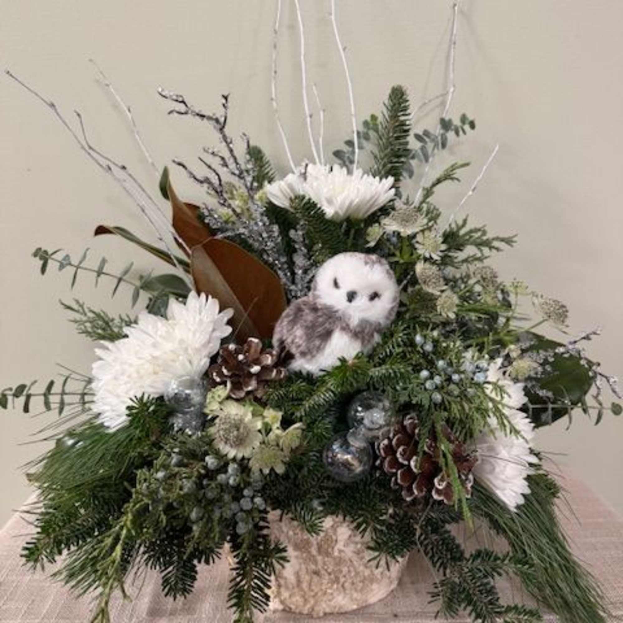 Winter floral arrangement with white blooms, pinecones, and a small owl figurine