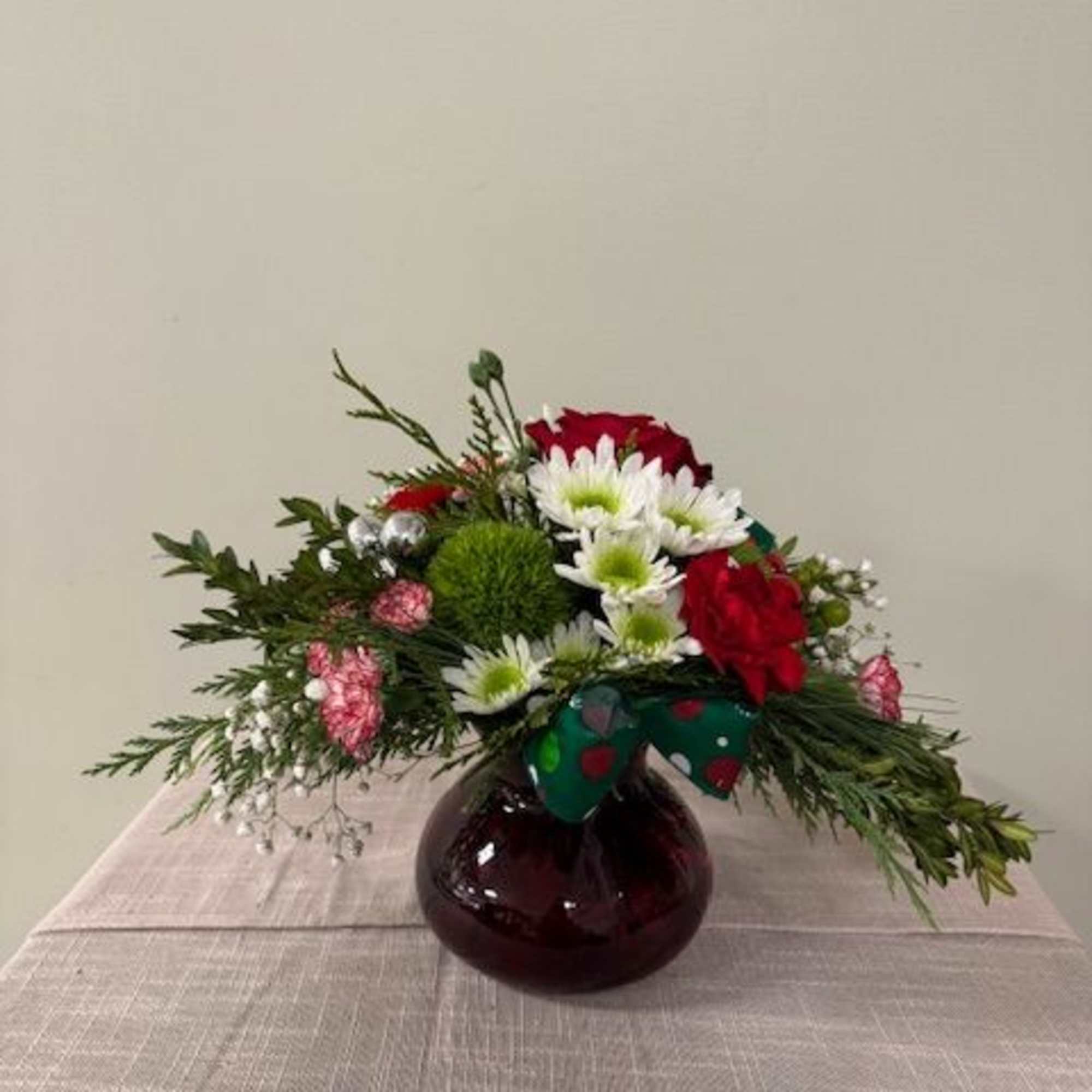 Red roses and white daisies in a round glass vase with a bow