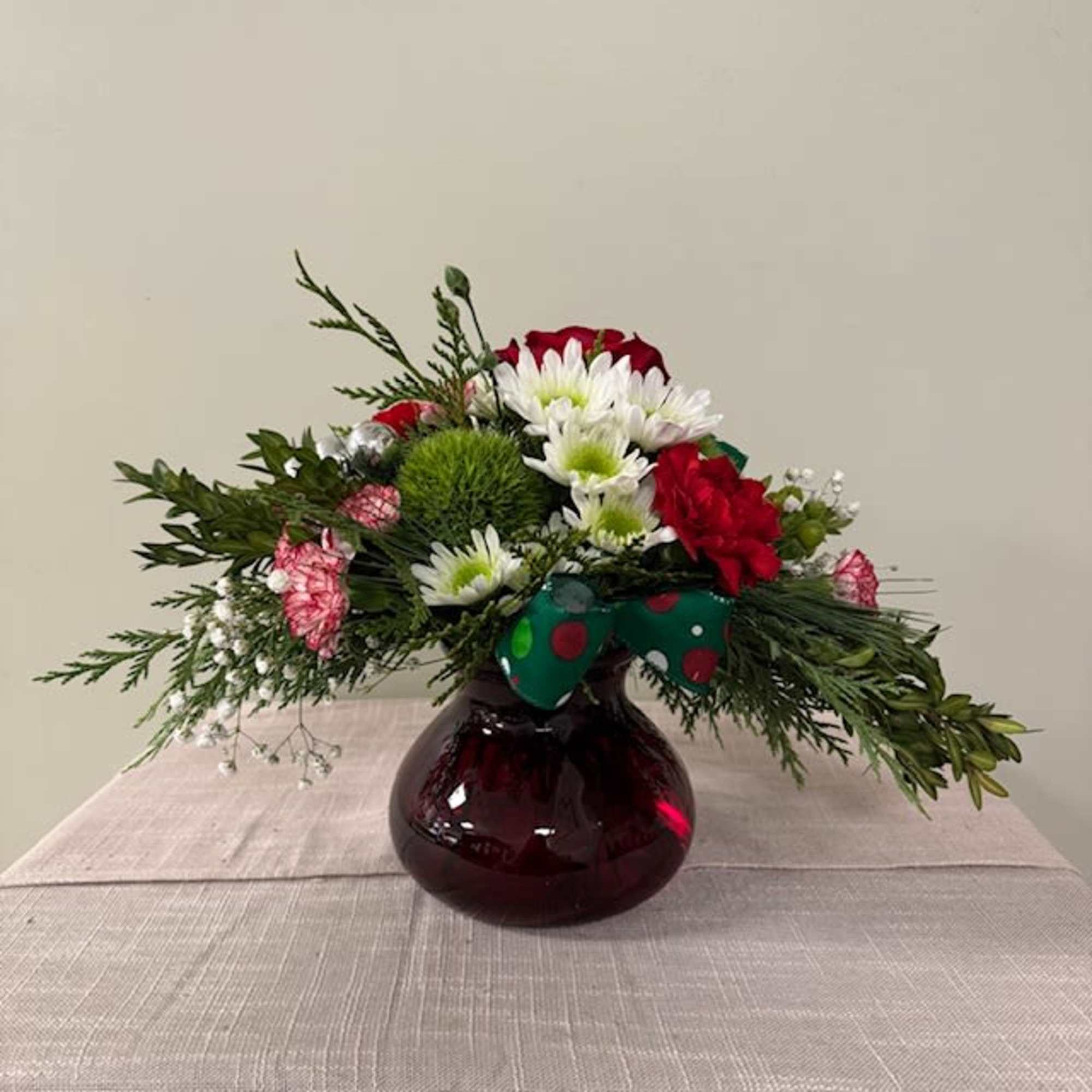 Red and white flowers arranged in a burgundy vase with a polka-dot bow