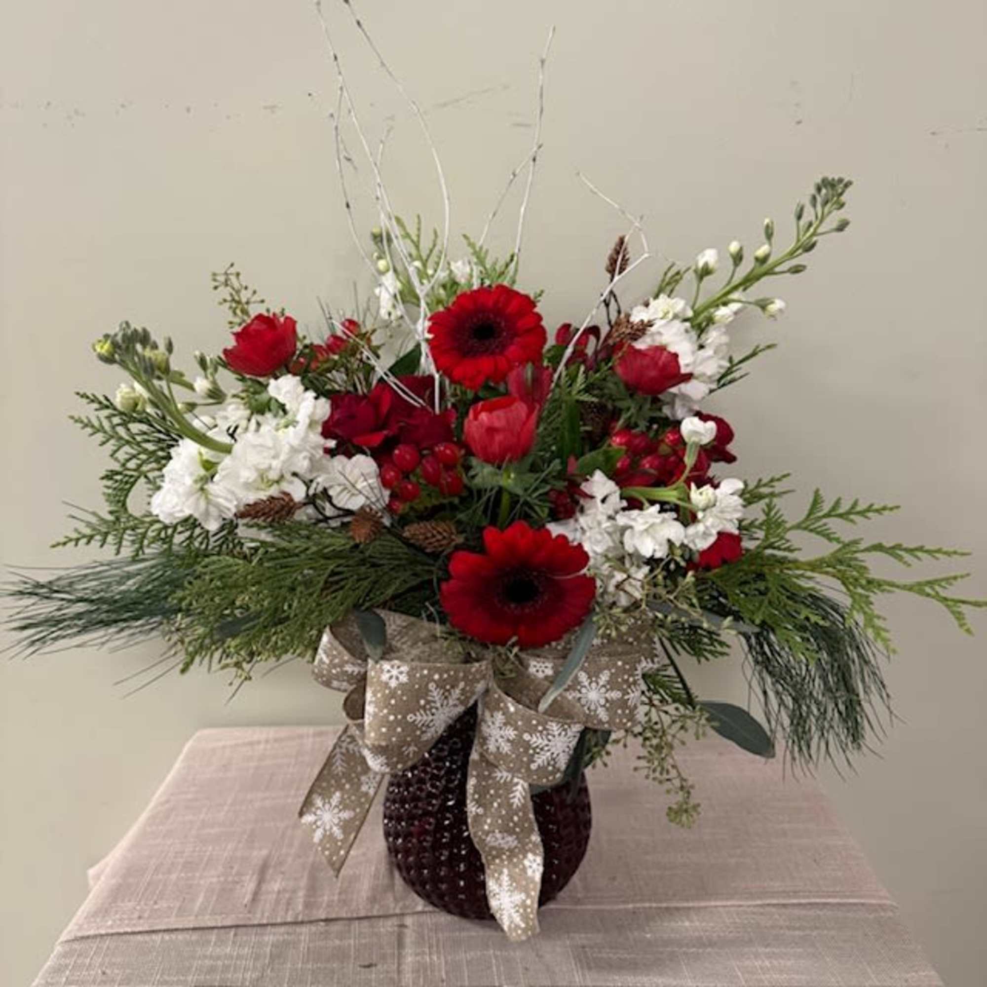 Red and white floral arrangement in a dark vase with a snowflake ribbon