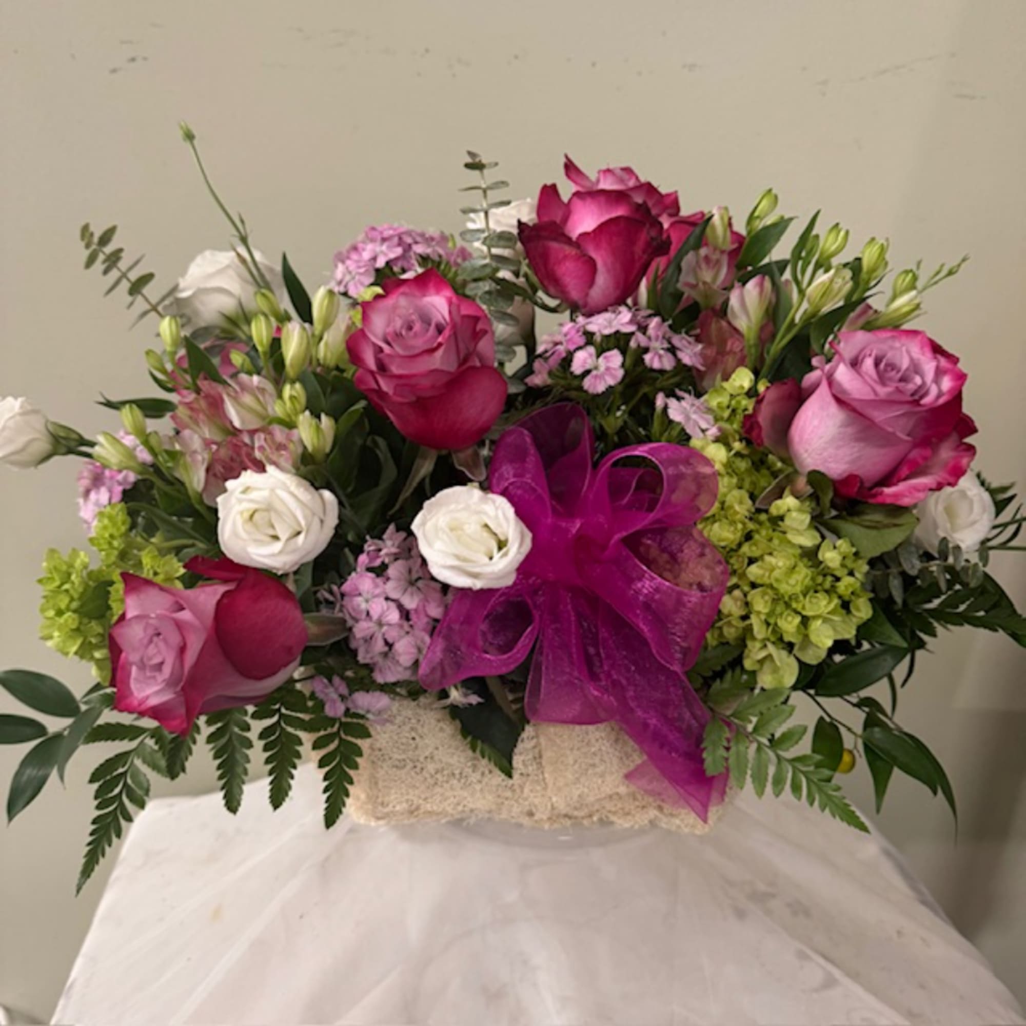 Bouquet of pink and white roses with a purple ribbon in a textured container