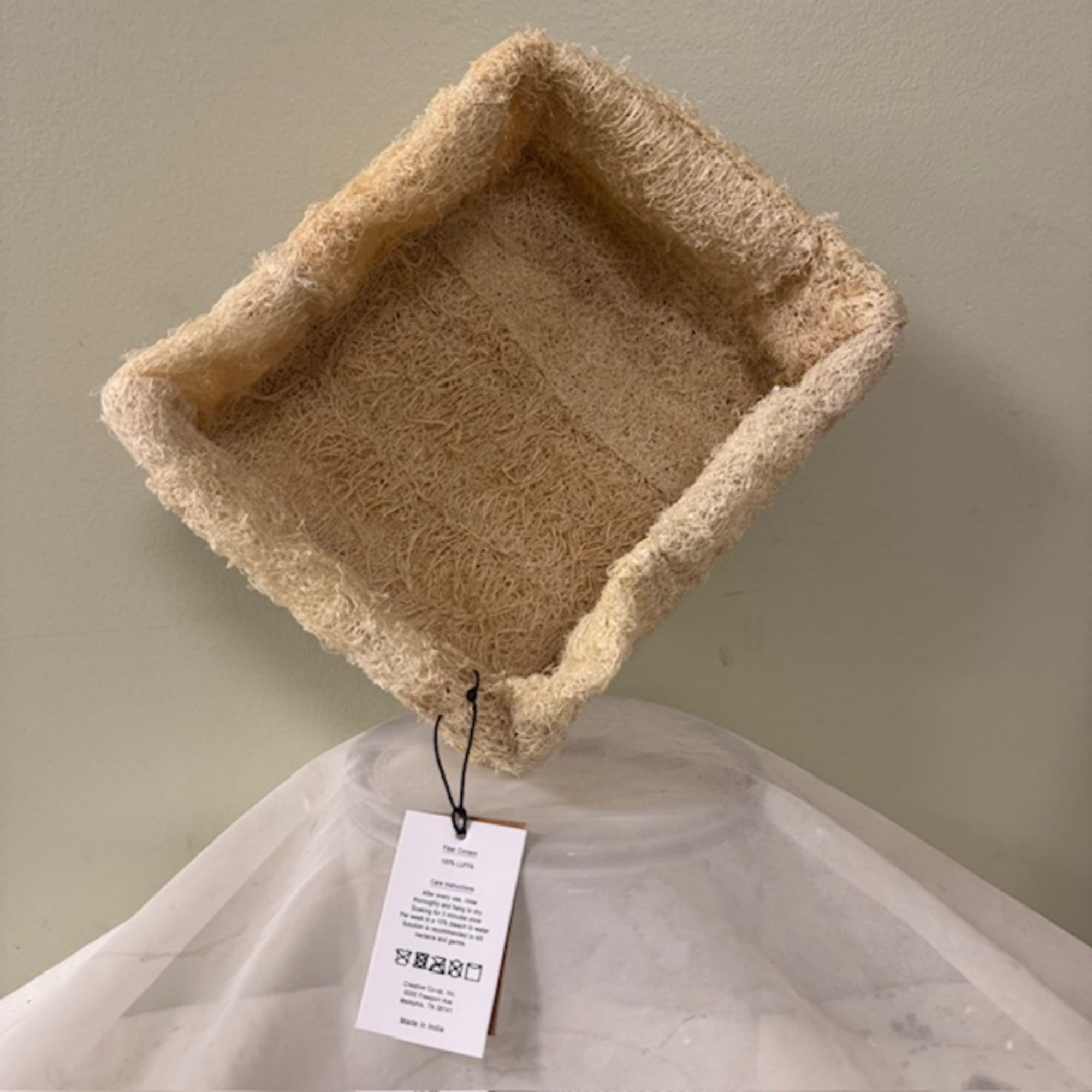 Empty square woven basket with a hanging tag on a draped white cloth