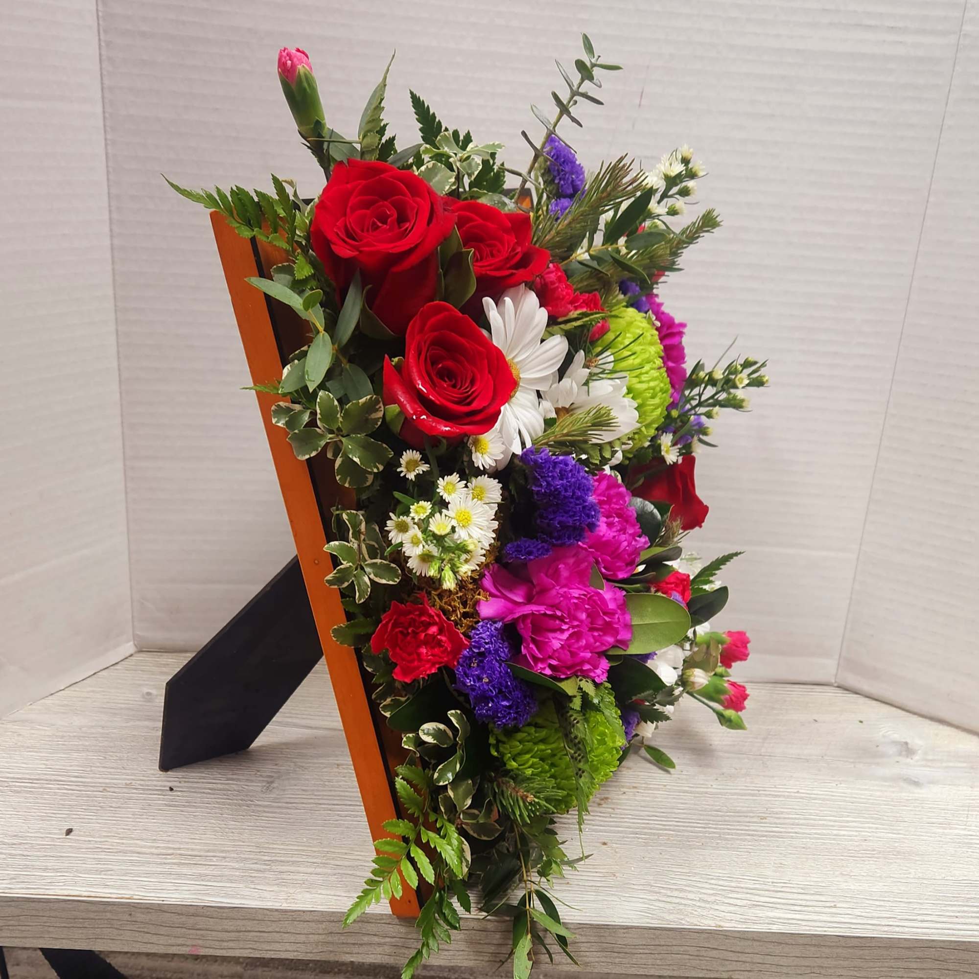 Mixed bouquet with red roses, pink carnations, and white daisies in a wooden holder