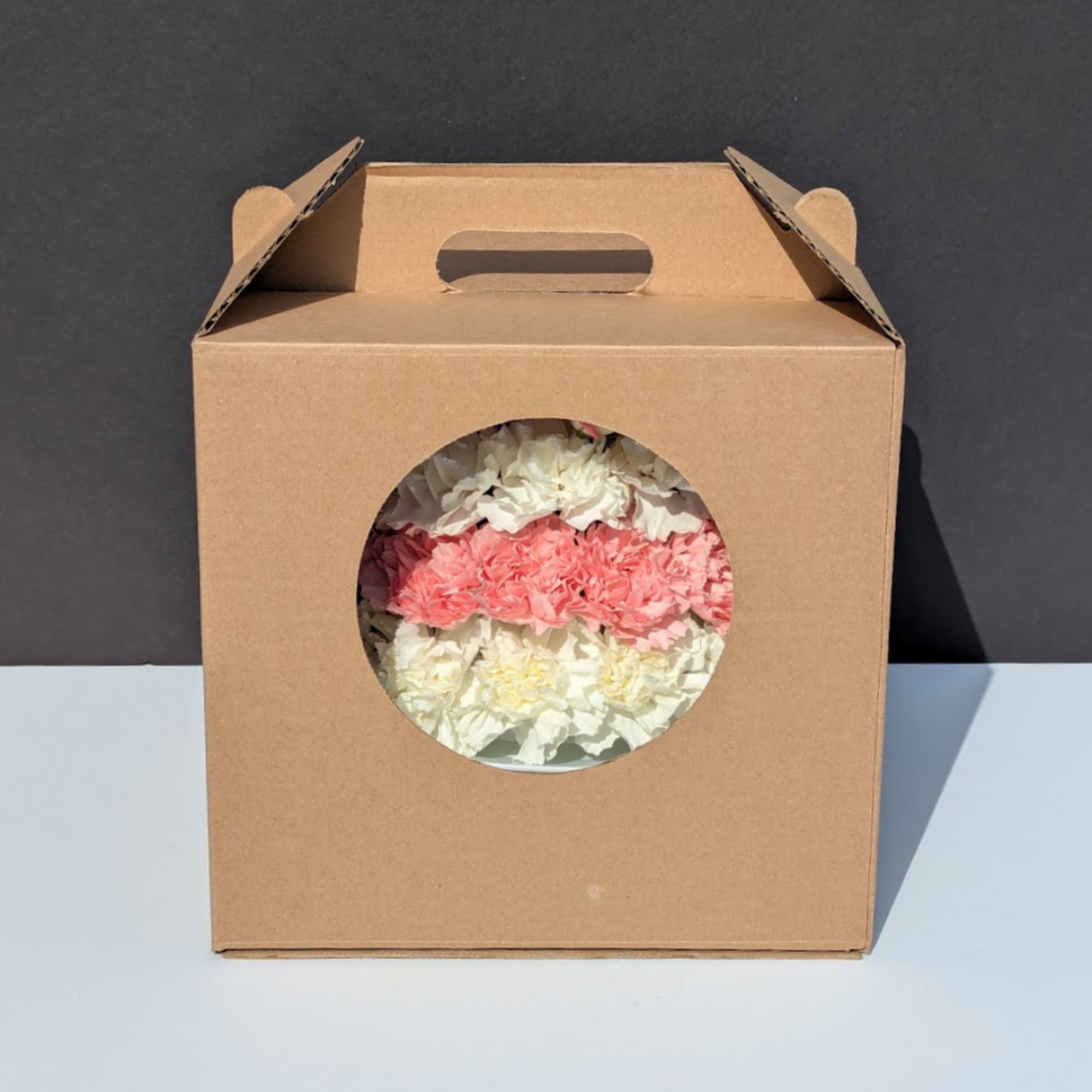 Cardboard gift box with pink and white carnations visible through a round window.