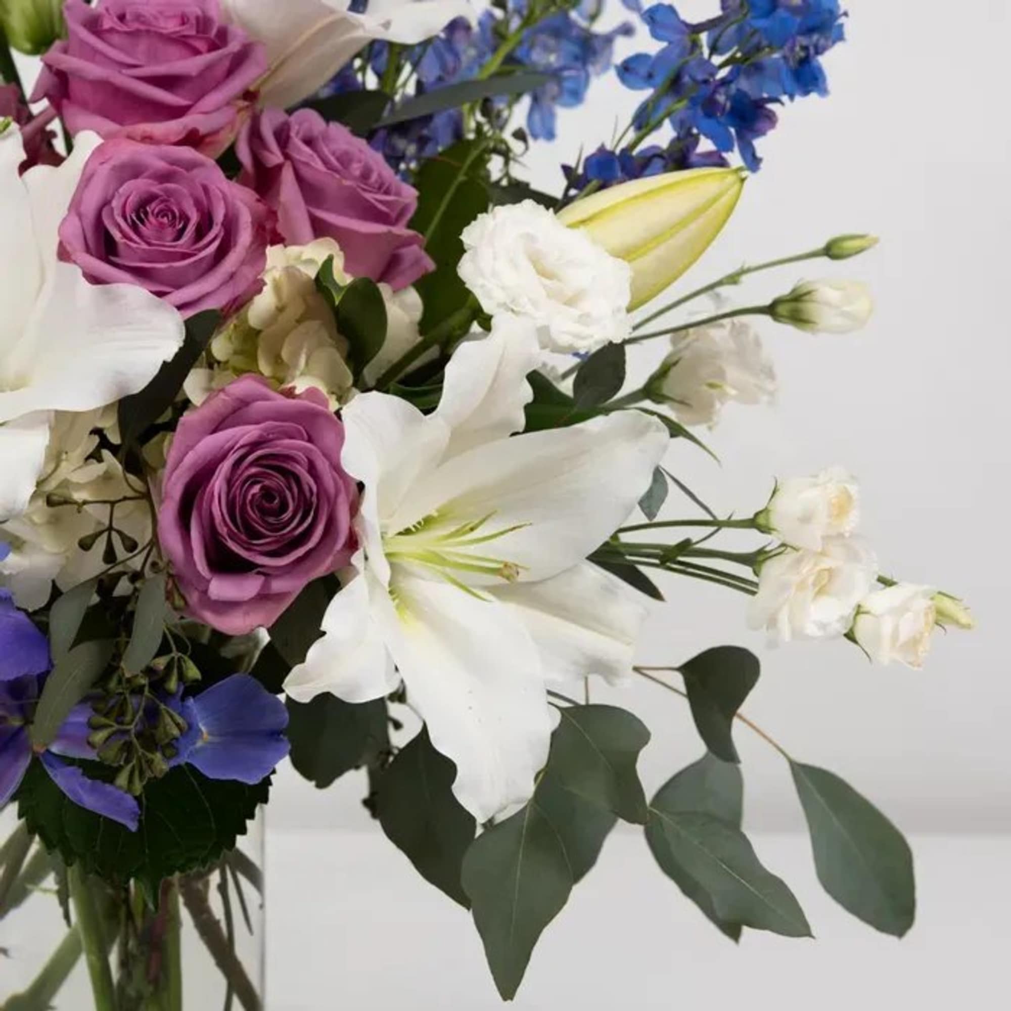 Bouquet of purple roses and white lilies with blue flowers in a glass vase