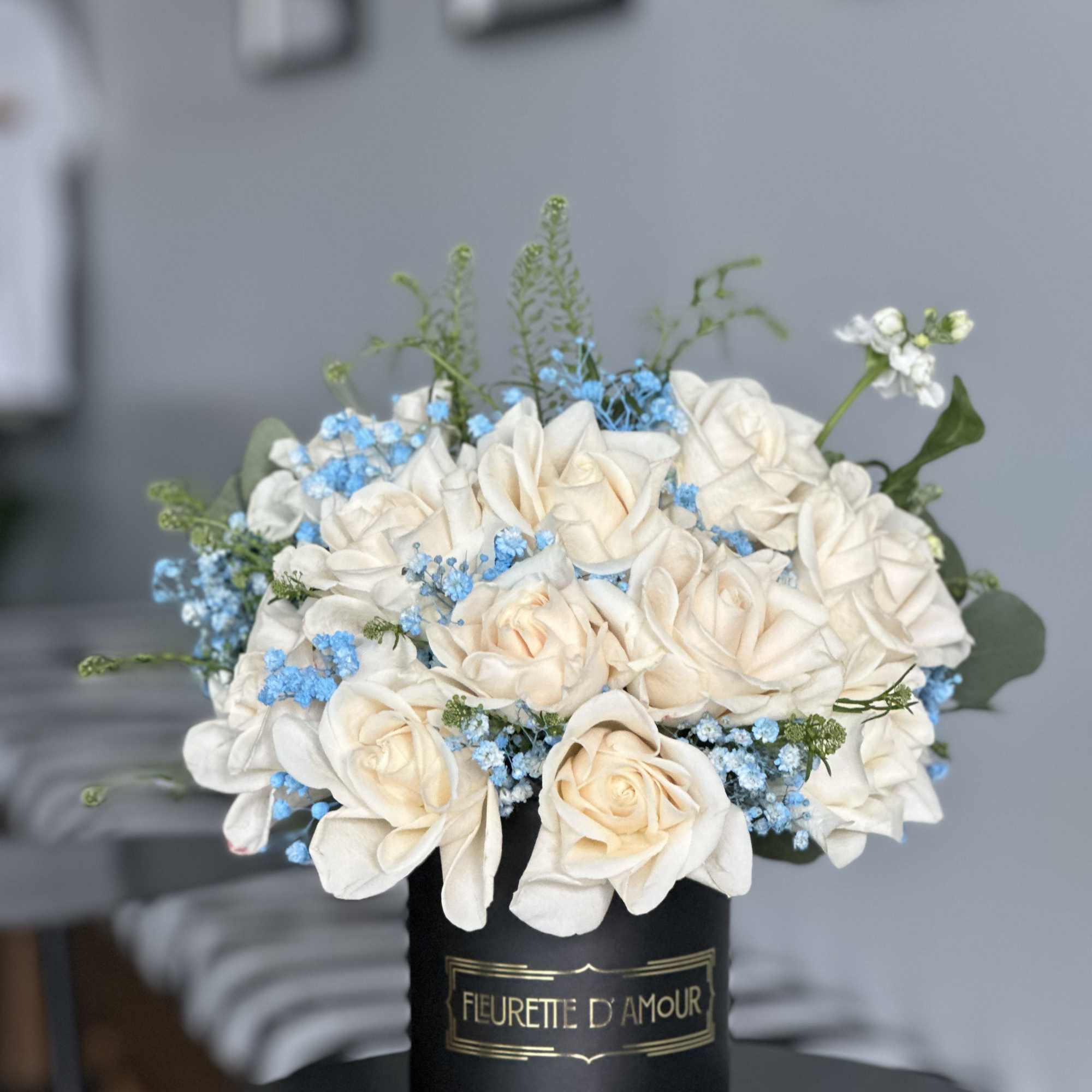 White roses and blue filler flowers arranged in a black hatbox