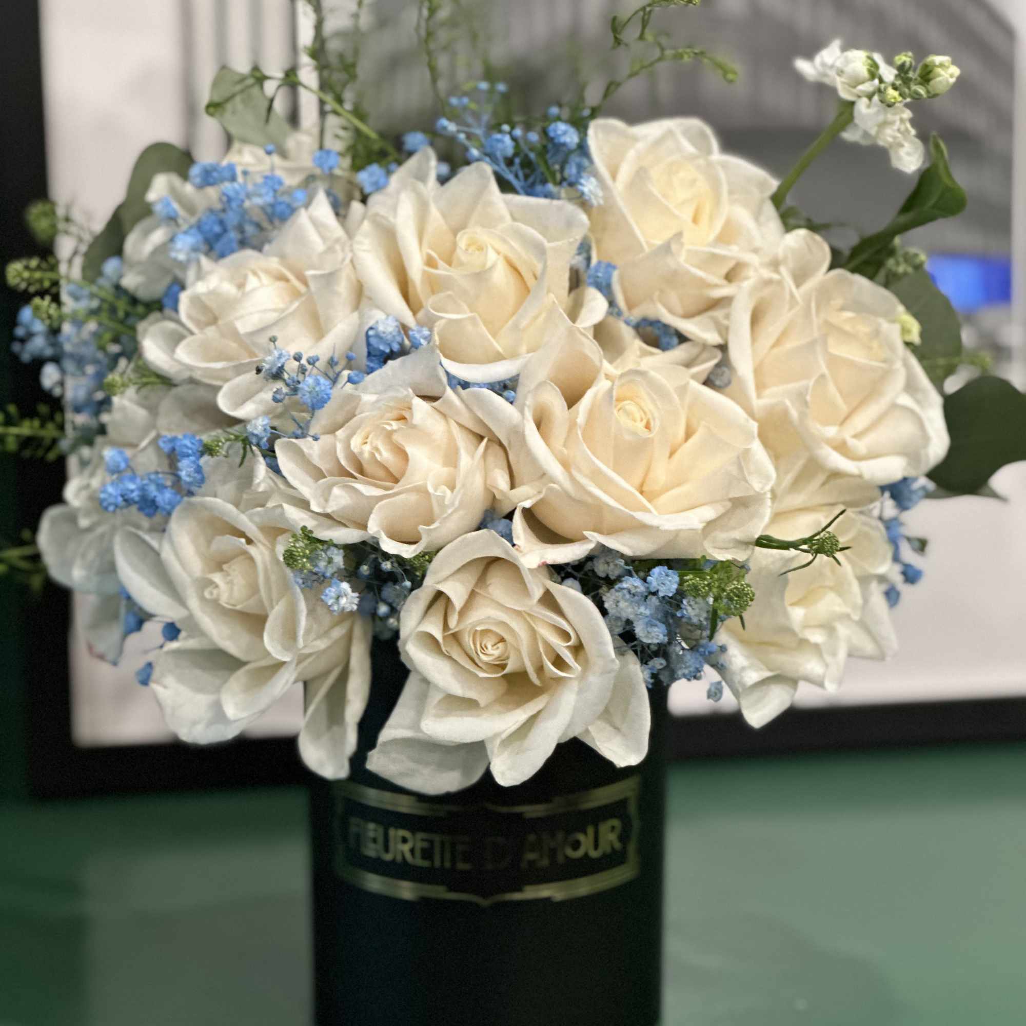 Cream roses with blue filler flowers in a black hatbox