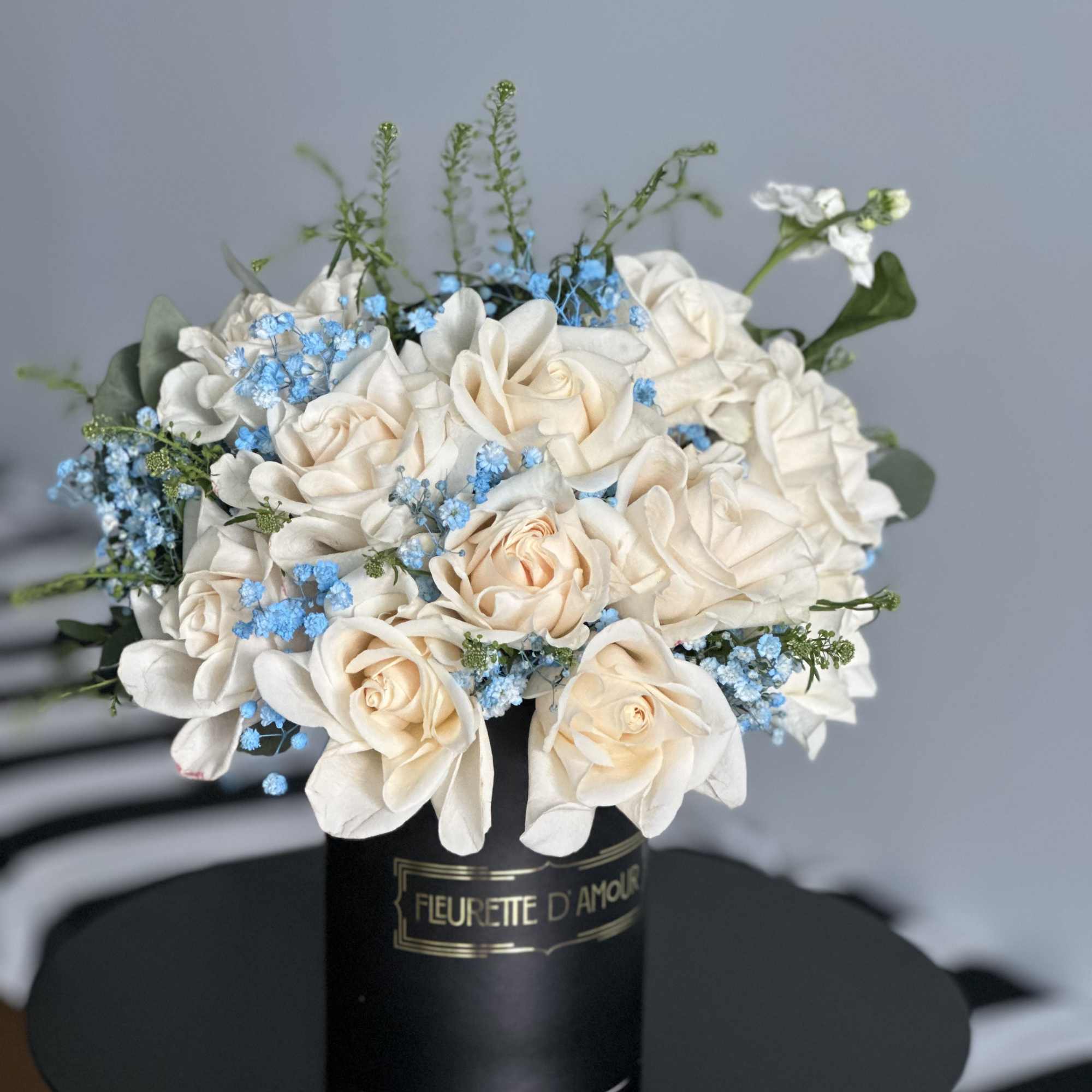 Cream roses and blue filler flowers in a black hatbox