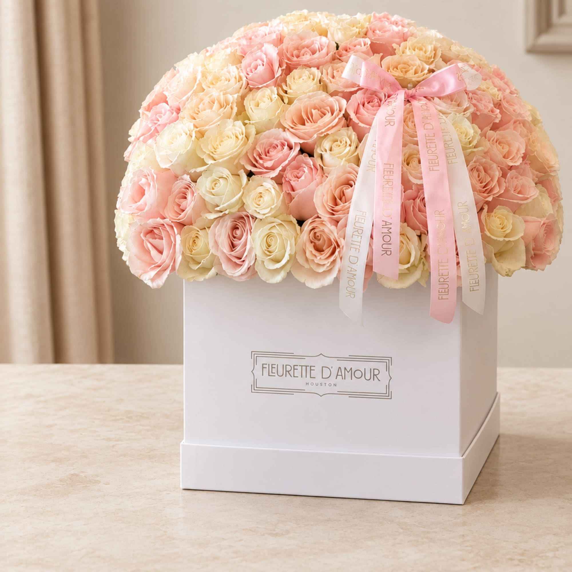 Pink and cream roses arranged in a white gift box with ribbon