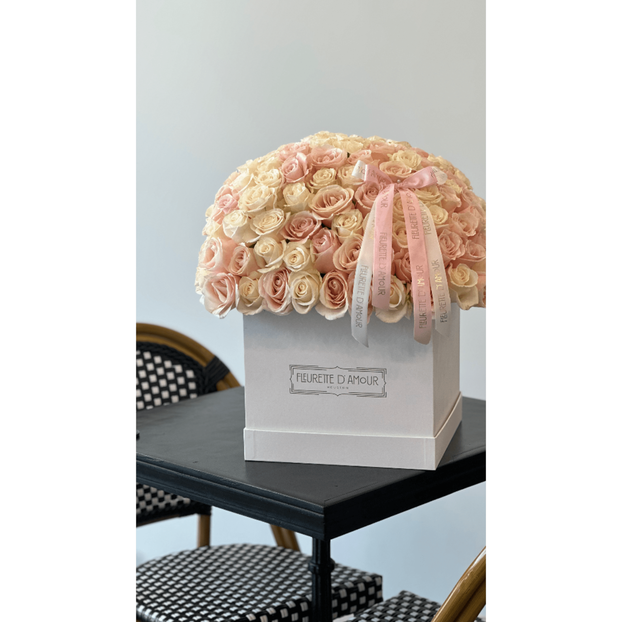 Cream and blush roses arranged in a white hat box with pink ribbons