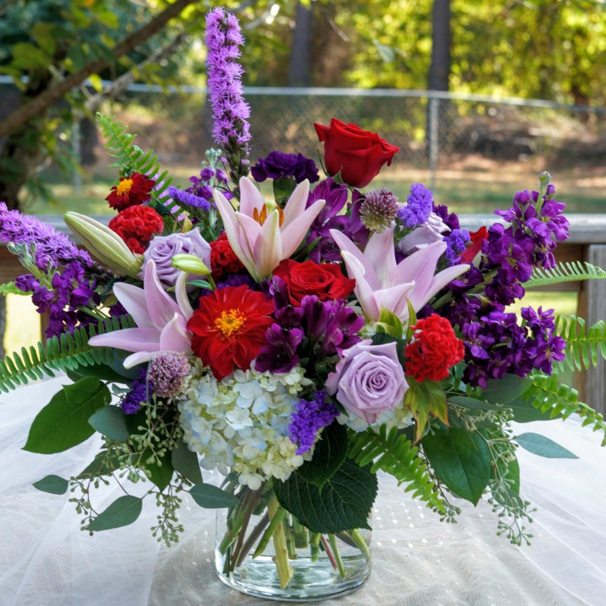 Bouquet of pink lilies, red roses, and purple flowers in a glass vase