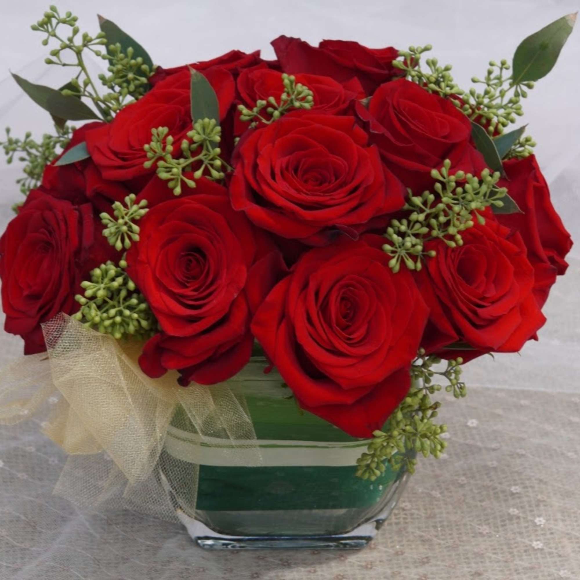 Red roses arranged in a square glass vase with a sheer ribbon bow