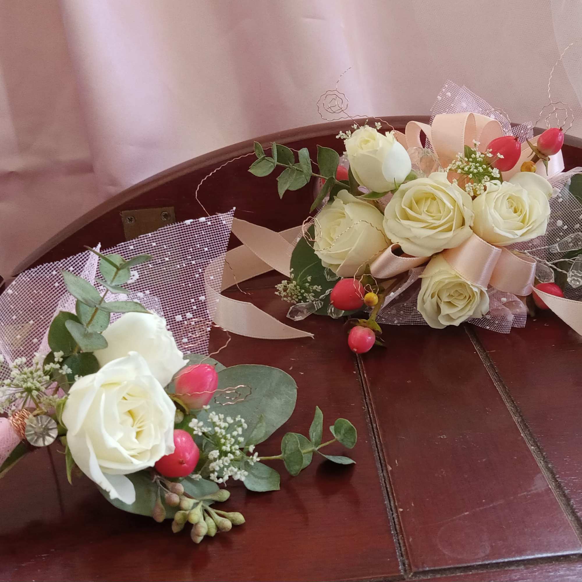 Two small rose bouquets with pink ribbon and greenery on a wooden bench