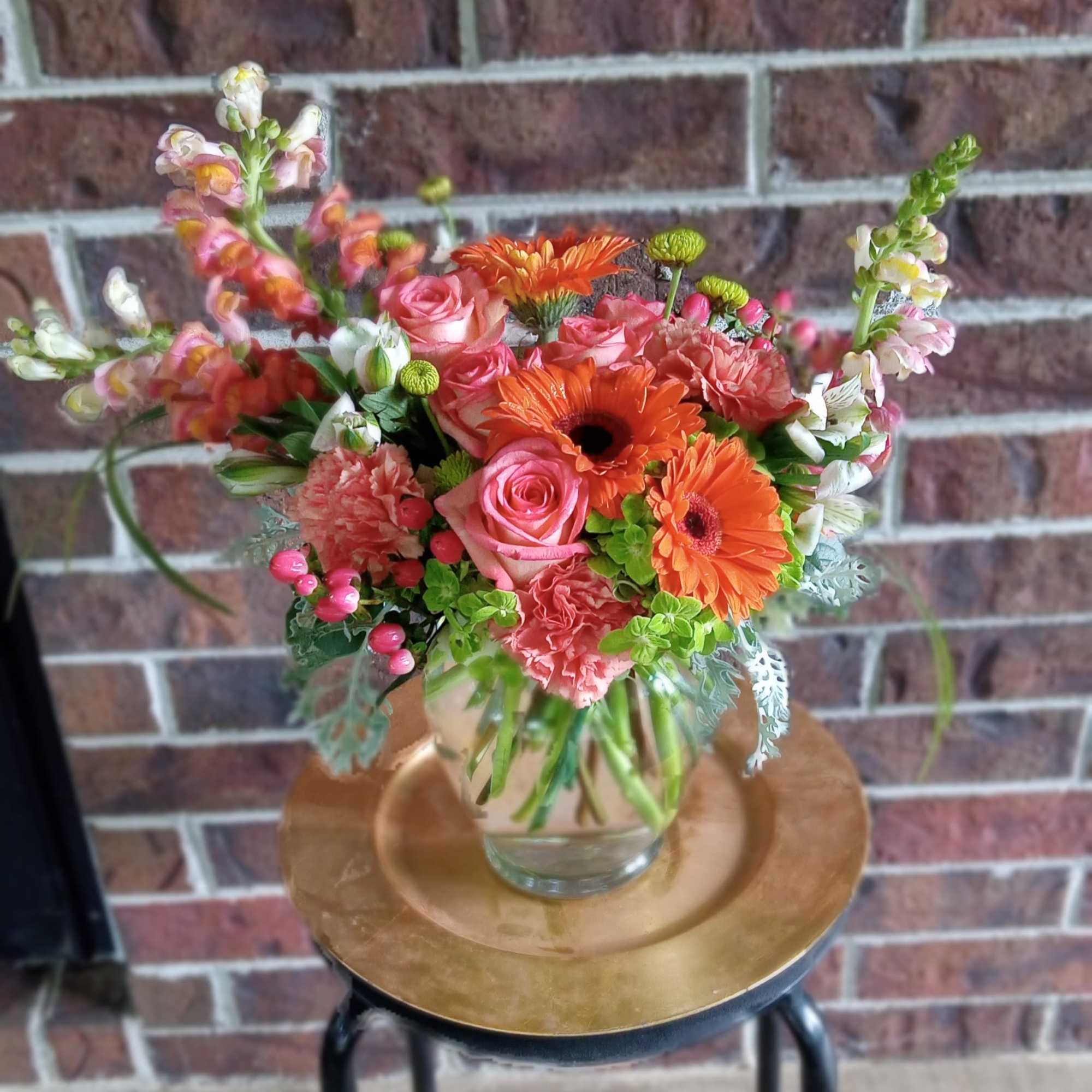 Mixed bouquet of orange and pink flowers in a clear glass vase