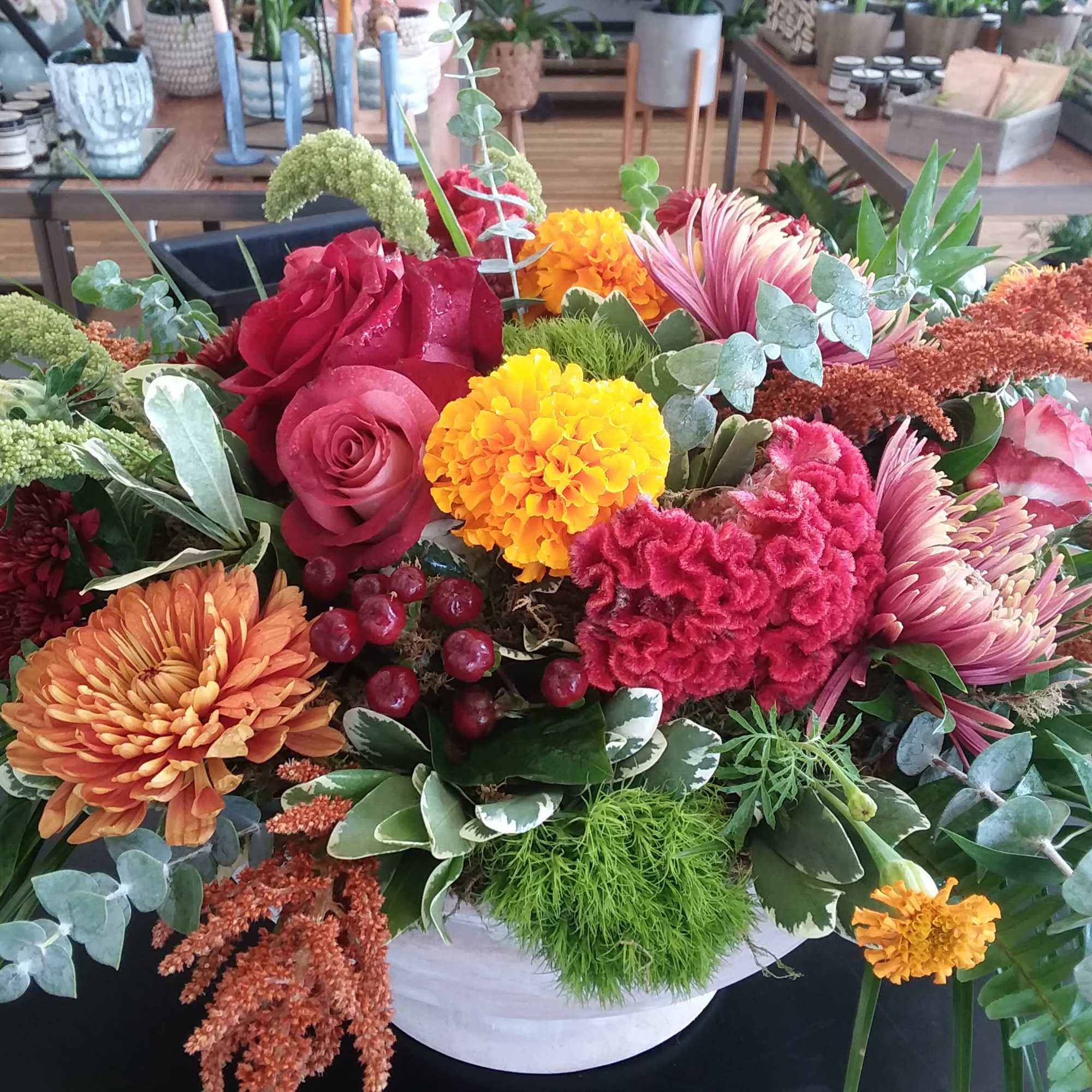 Mixed bouquet with roses, chrysanthemums, and bright fall flowers in a white container