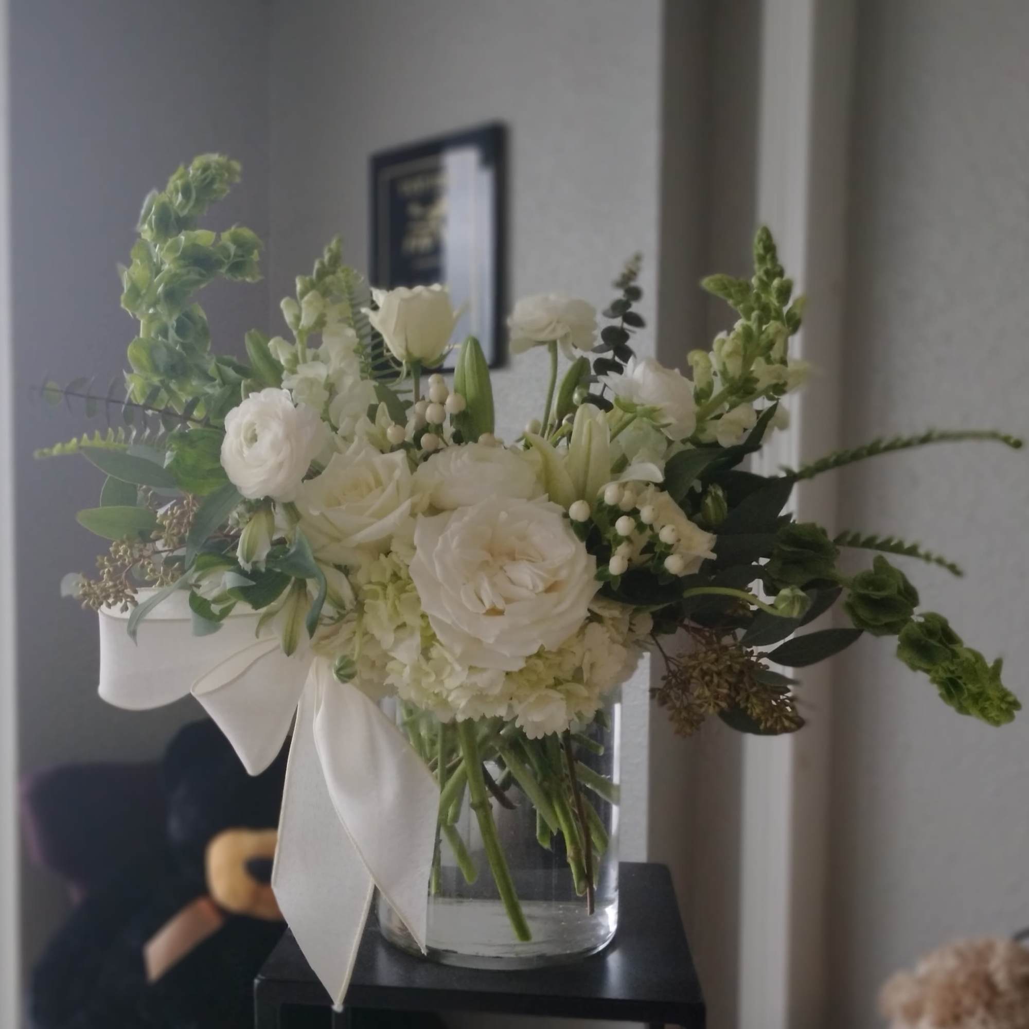 White floral arrangement in a clear glass vase with a satin ribbon