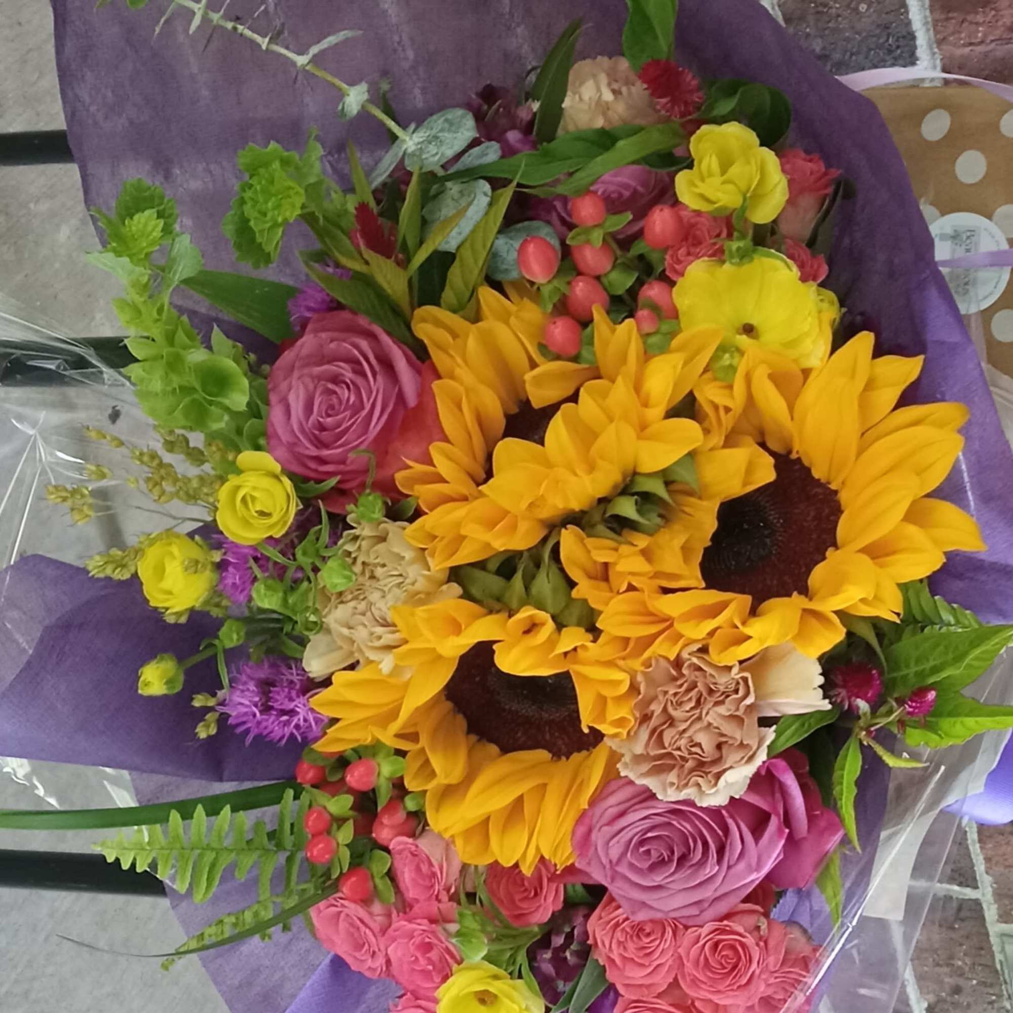 Bouquet with sunflowers, roses, and carnations wrapped in purple paper