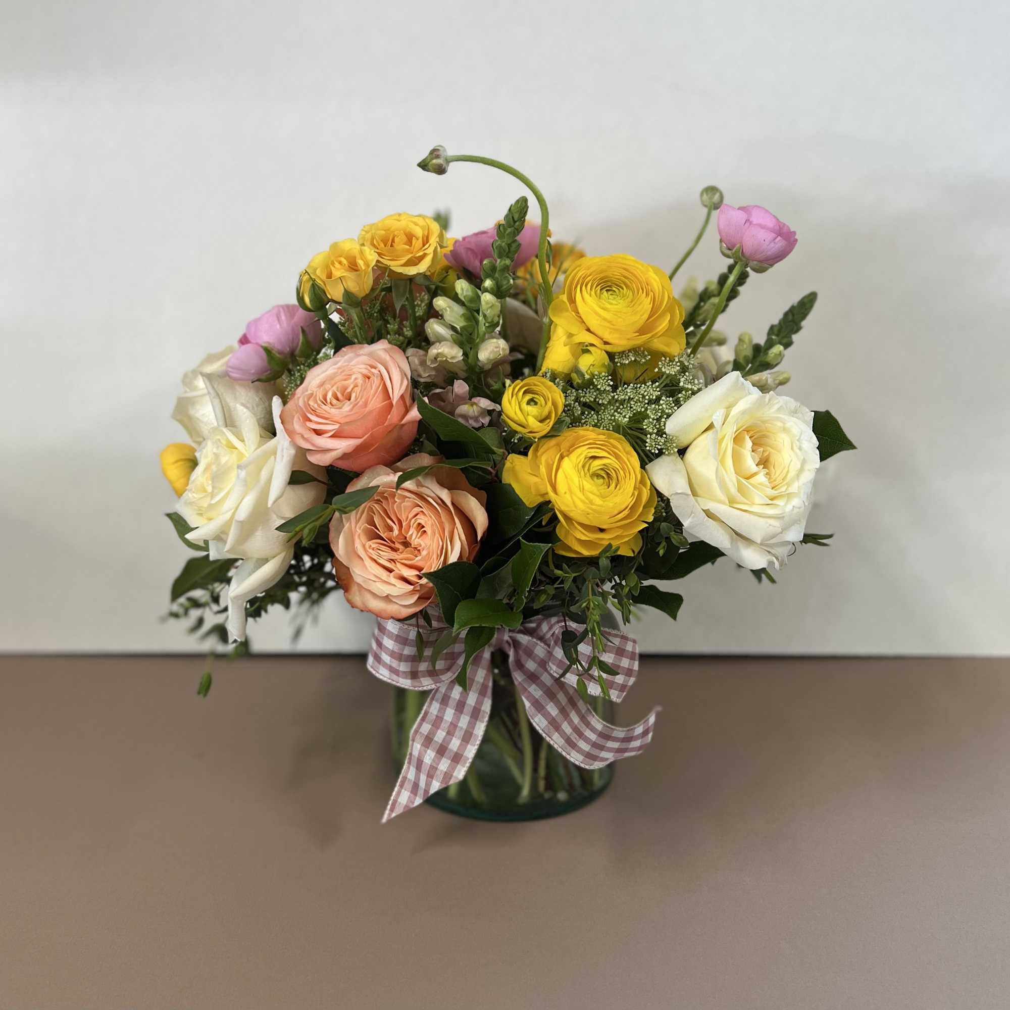 Mixed bouquet of roses and ranunculus in a glass vase with a gingham ribbon