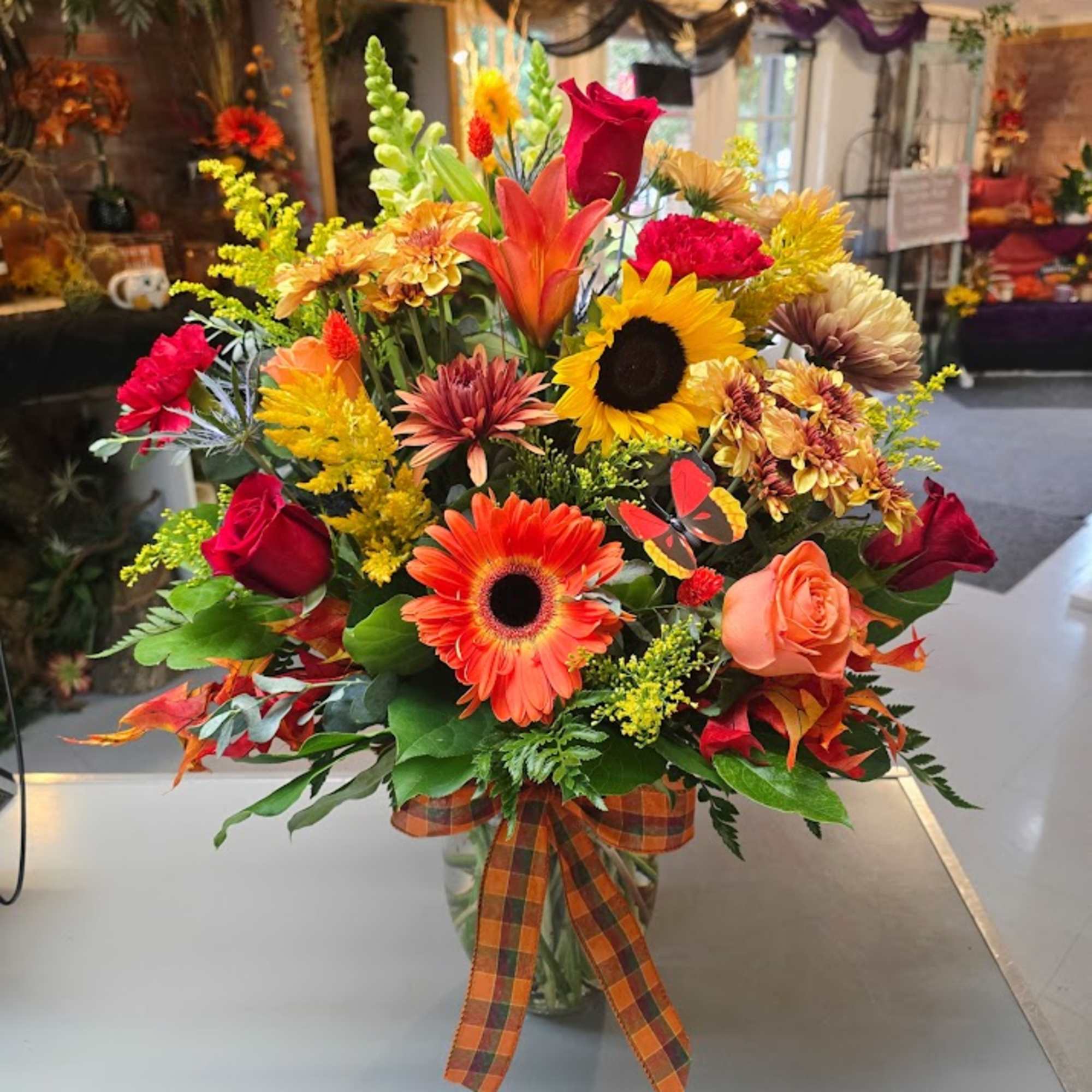 Autumn bouquet with sunflowers, roses, and gerbera daisies in a glass vase