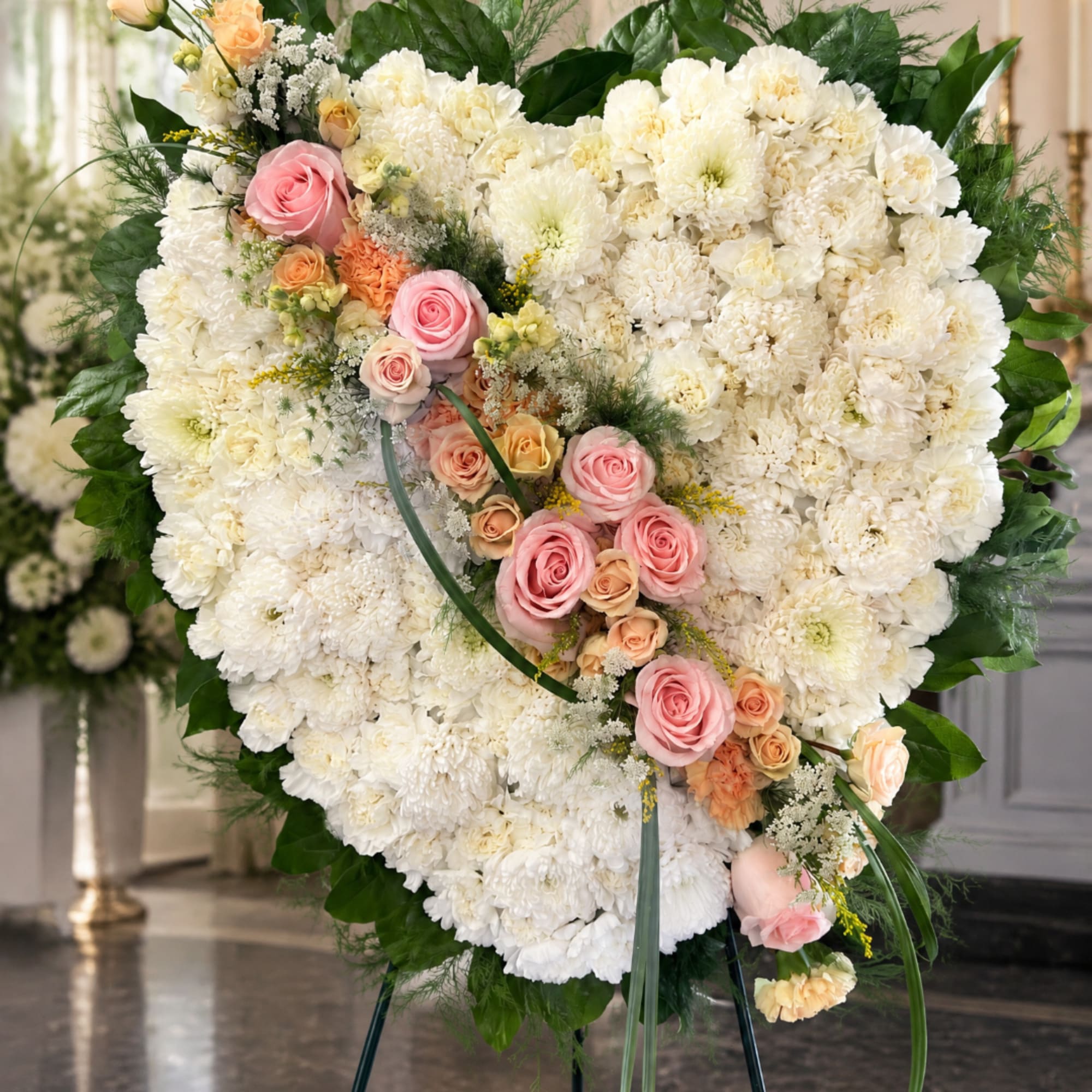 Heart-shaped white floral standing spray with pink roses and peach accents