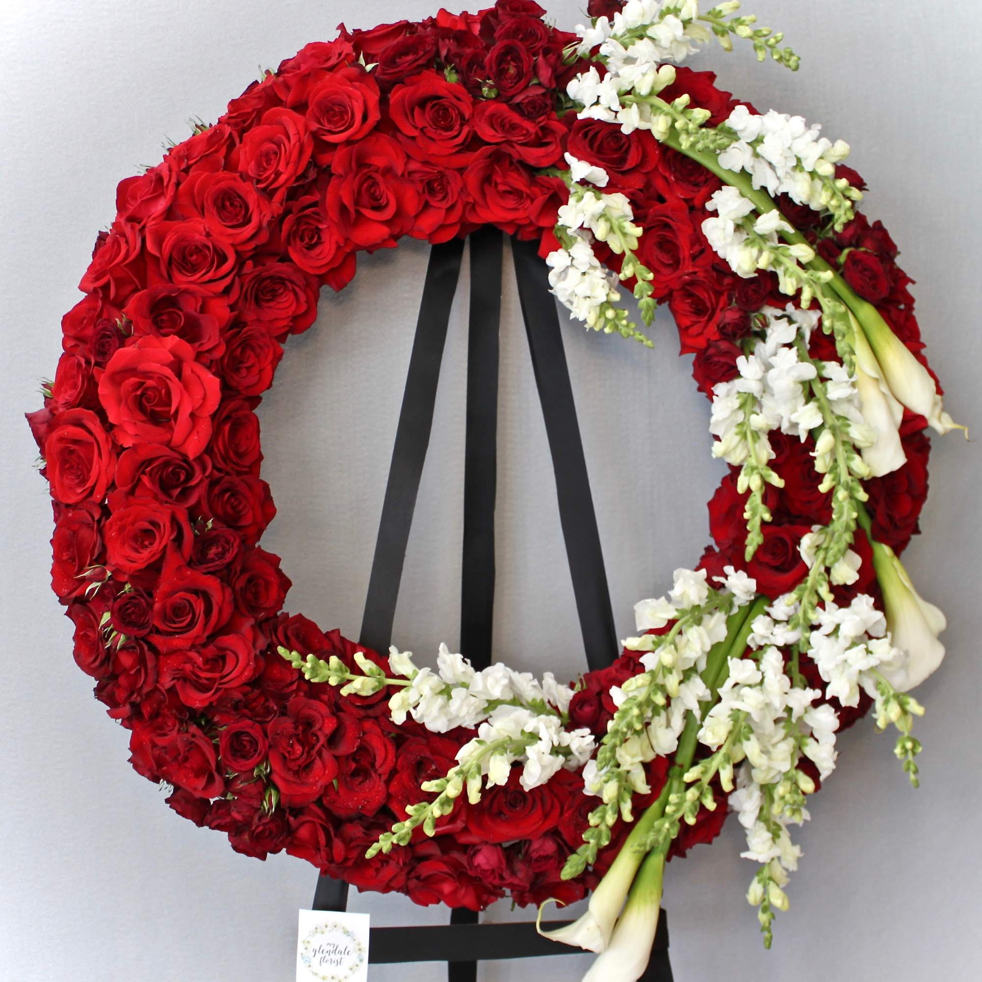Covered in red roses, this wreath also includes calla lilies and snapdragons.