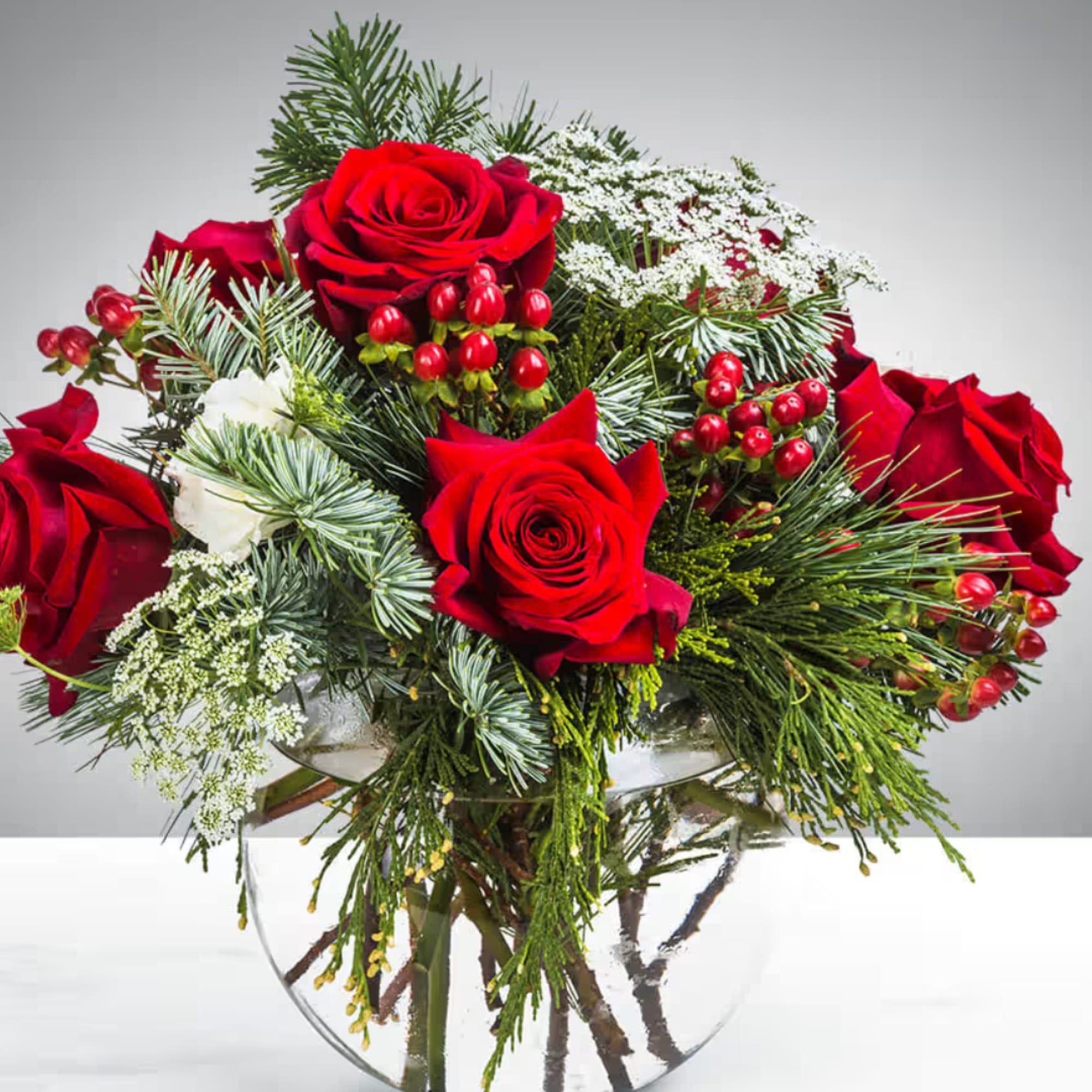 Red roses and white flowers in a clear glass vase with evergreen accents
