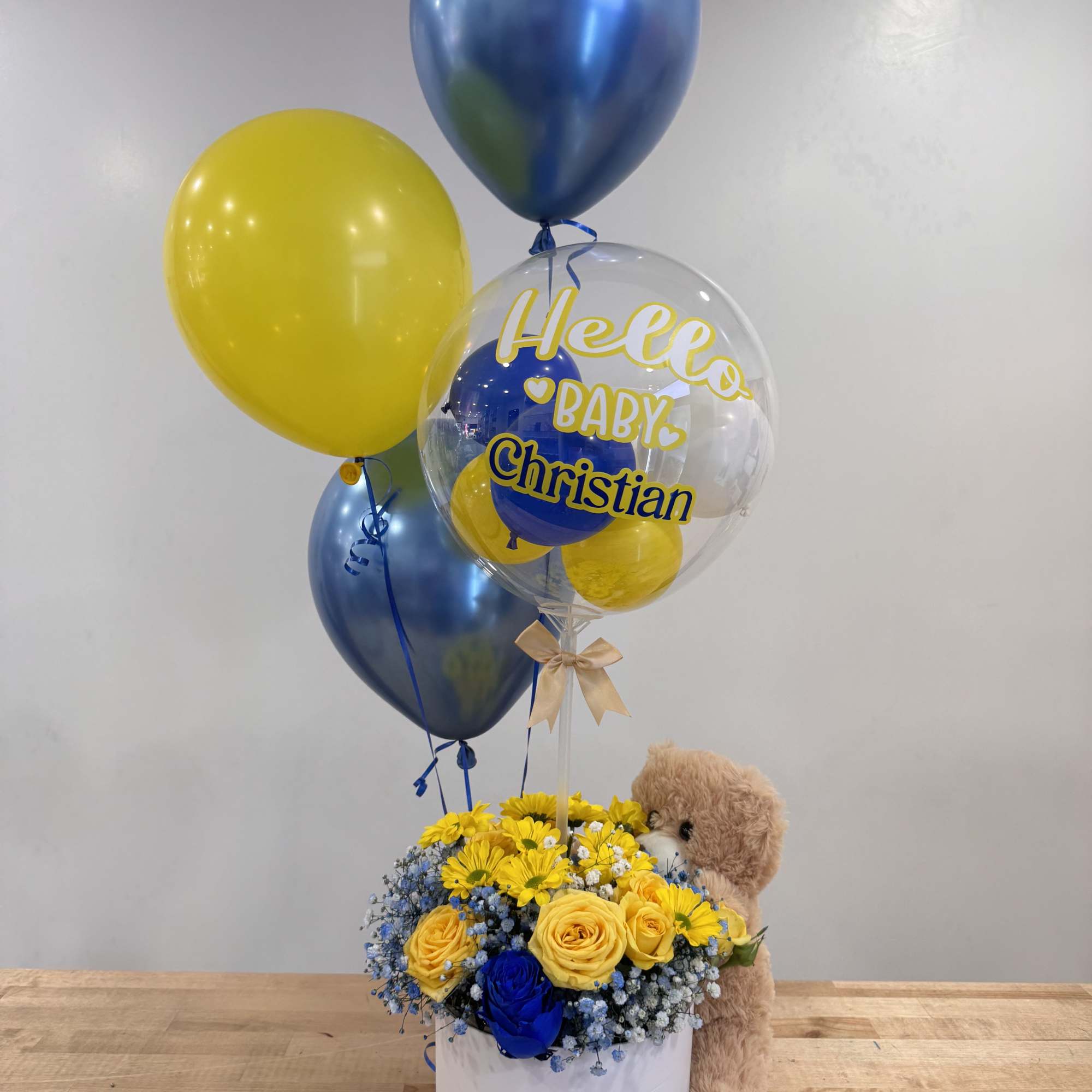 Blue and yellow flower hat box with baby-themed balloons and a teddy bear.