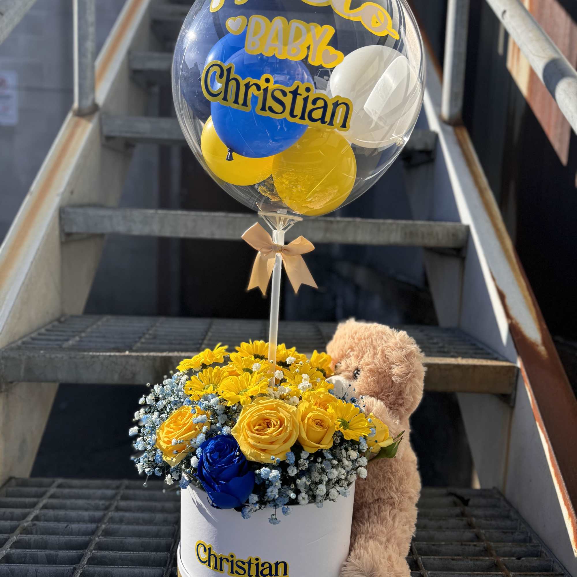 Hatbox of yellow and blue flowers with a bubble balloon and teddy bear labeled for baby Christian.