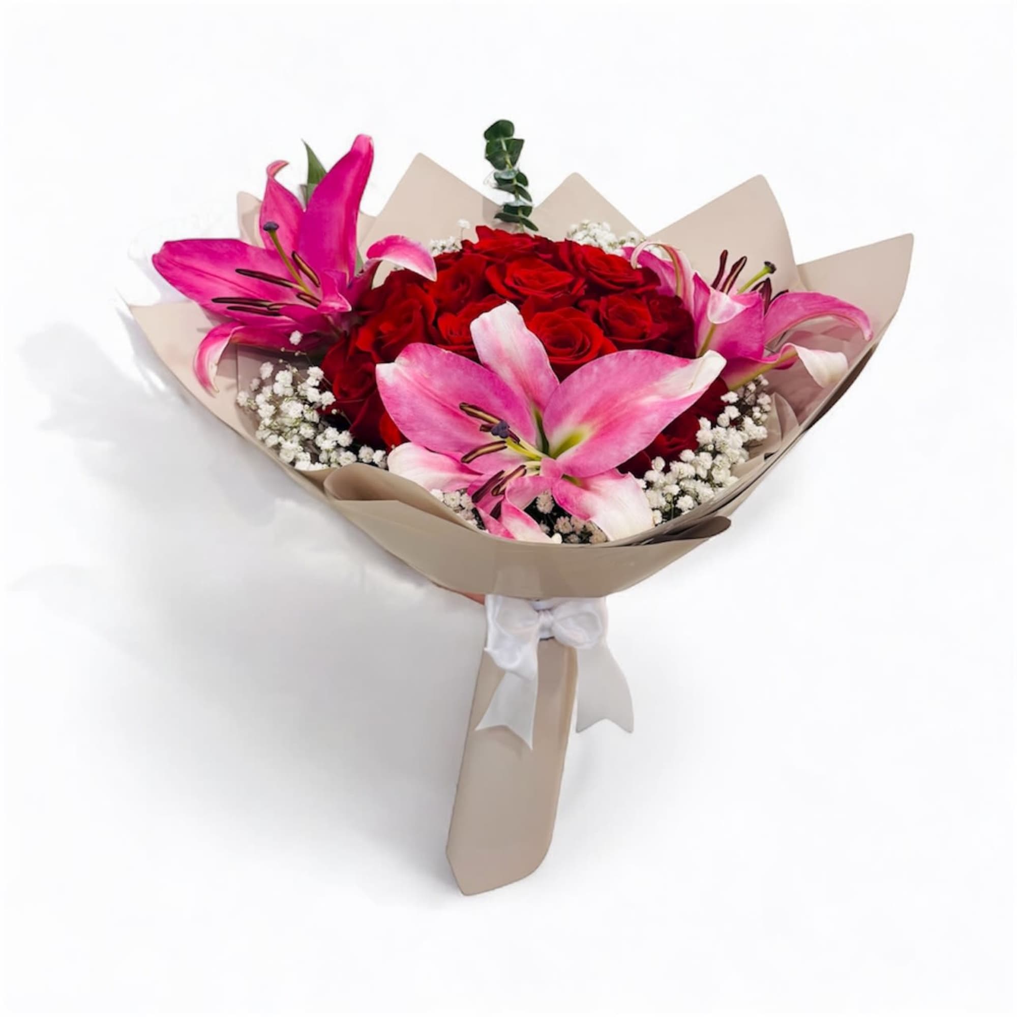 Hand-tied bouquet of red roses and pink lilies wrapped in beige paper with a white ribbon.