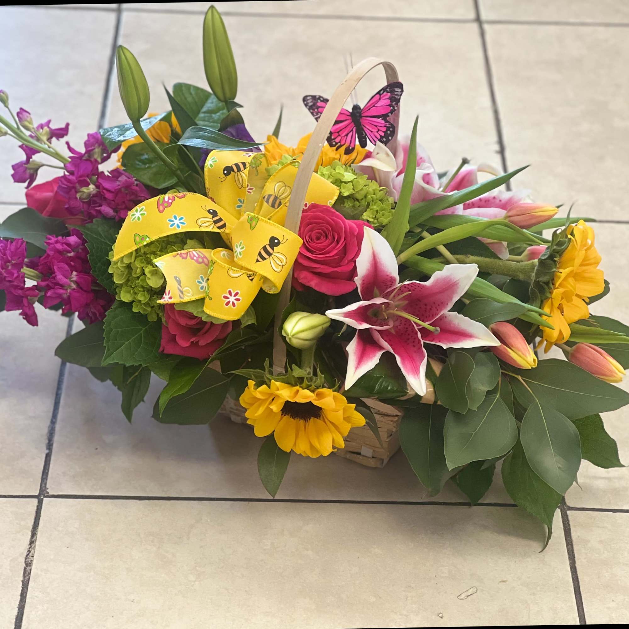 Basket arrangement with pink roses, lilies, sunflowers, and a yellow ribbon