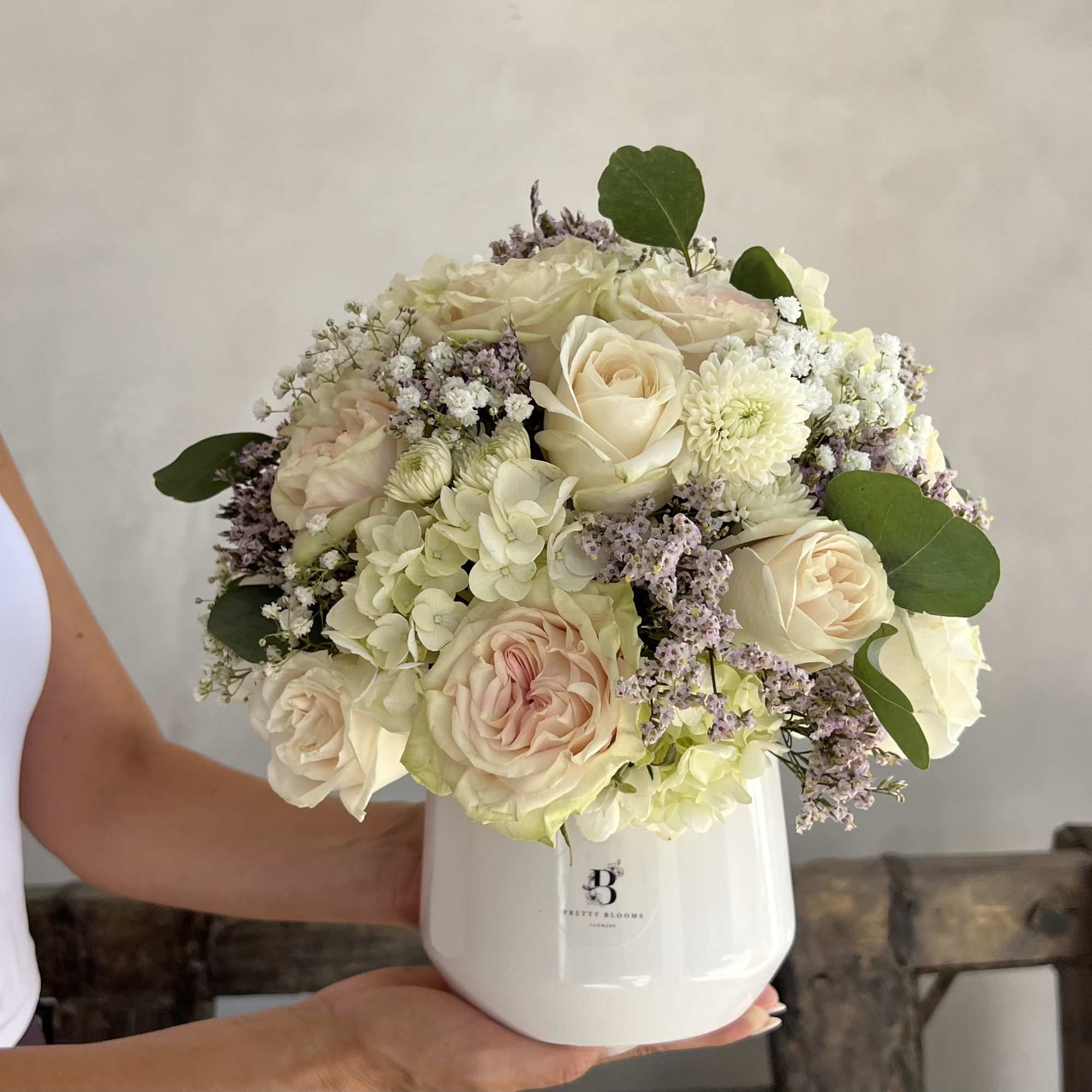 Cream roses and hydrangeas in a white vase with green leaves