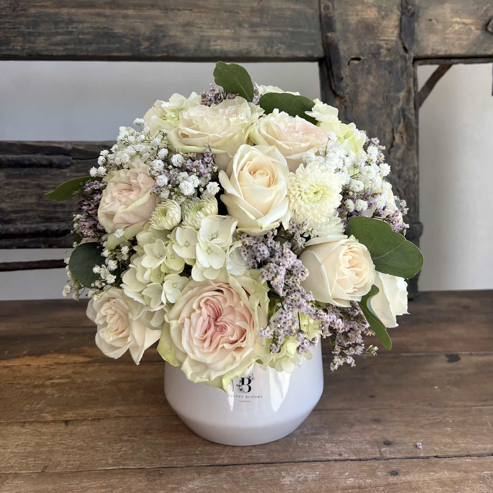 Cream rose bouquet in a white vase with pale filler flowers