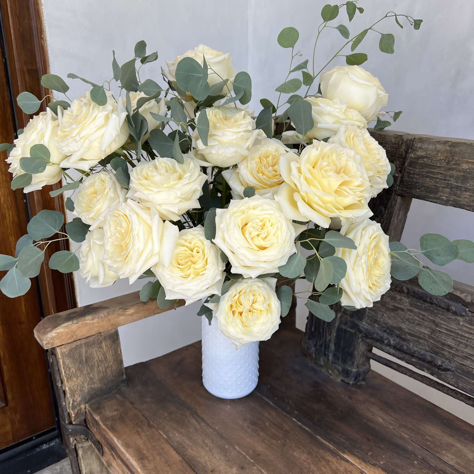 White roses arranged in a small vase with eucalyptus