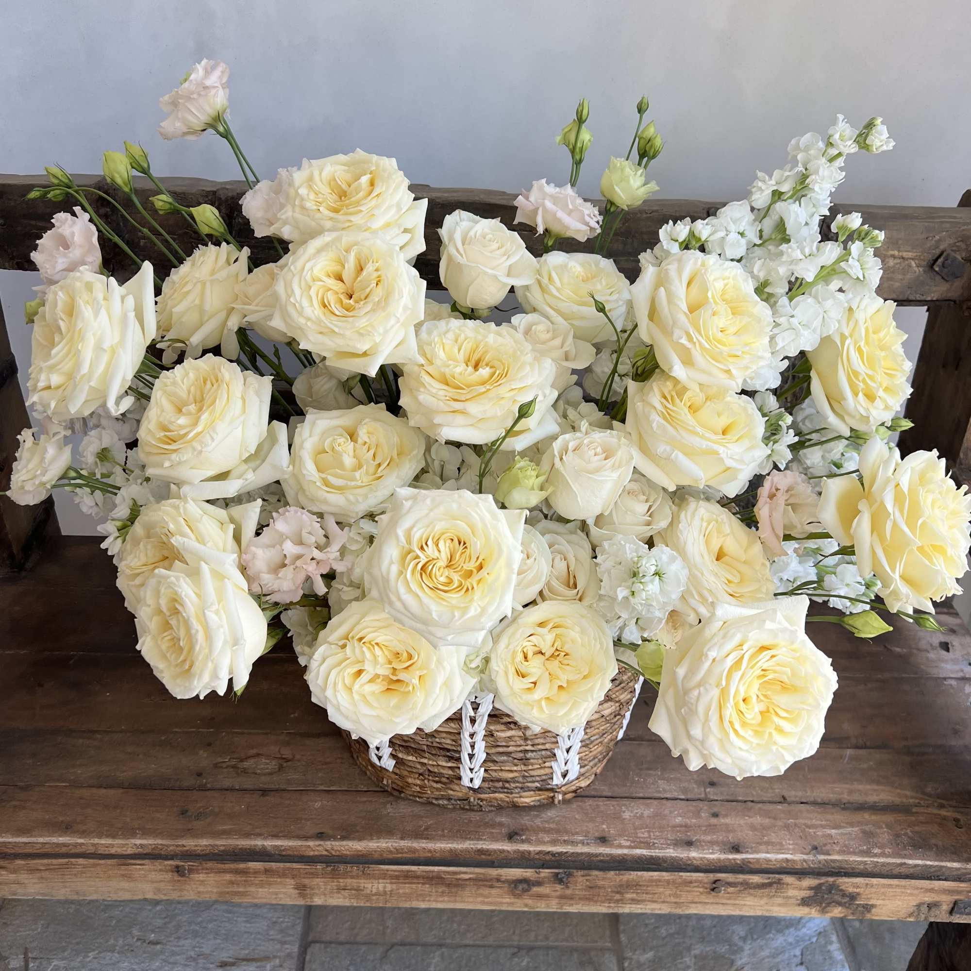 Cream roses arranged in a woven basket with white filler flowers