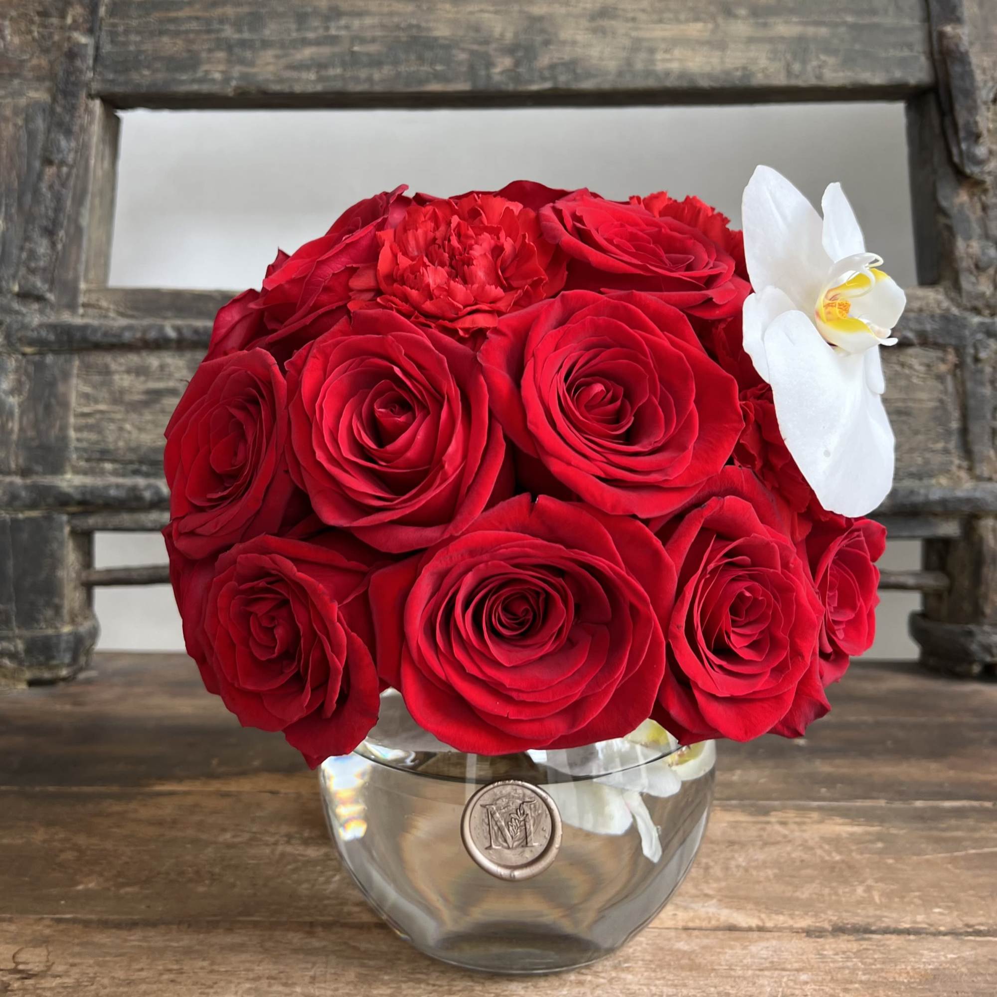 Red rose bouquet in a clear glass vase with a white orchid accent
