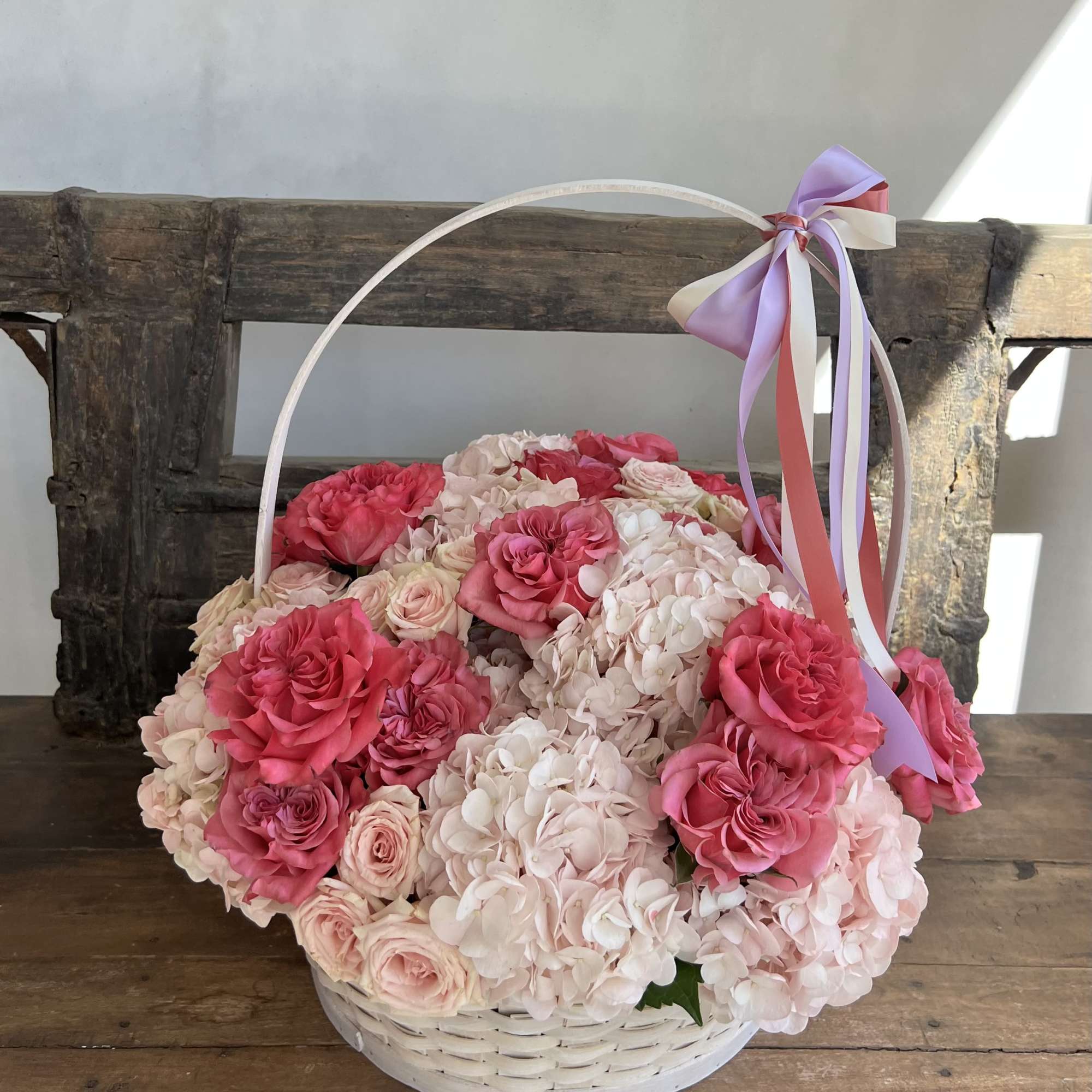 Basket of pink roses and pale hydrangeas with a ribbon handle